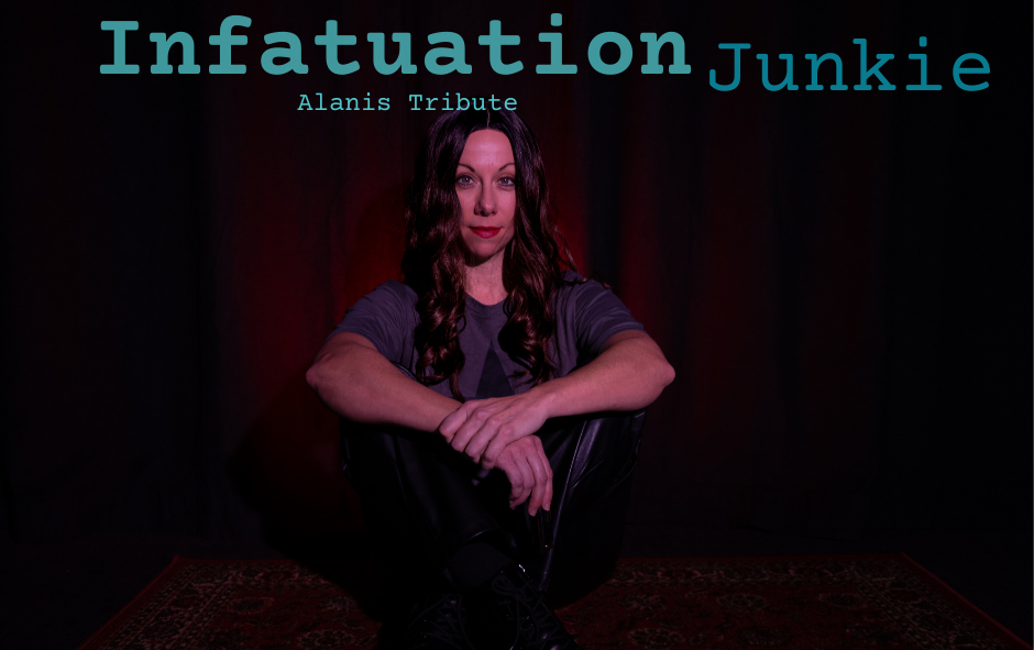 A woman with long wavy brown hair sitting on a dark rug, wearing a gray T-shirt and black pants, with a dark backdrop behind her, and text reading "Infatuation Junkie" and "Alanis Tribute" above her.