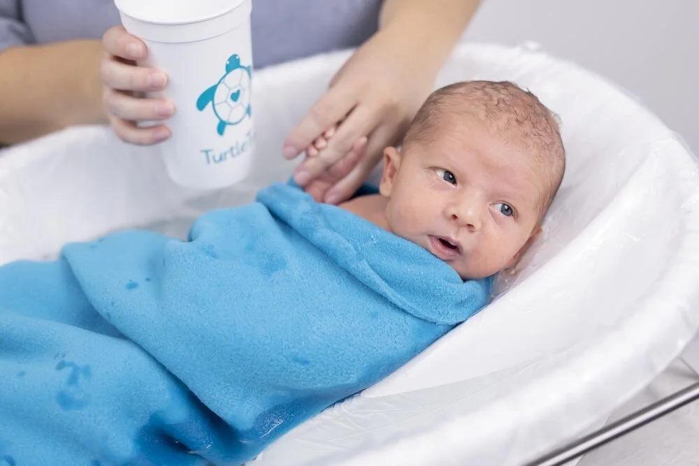 Baby in blue swaddling bathing blanket getting bath in TurtleTub