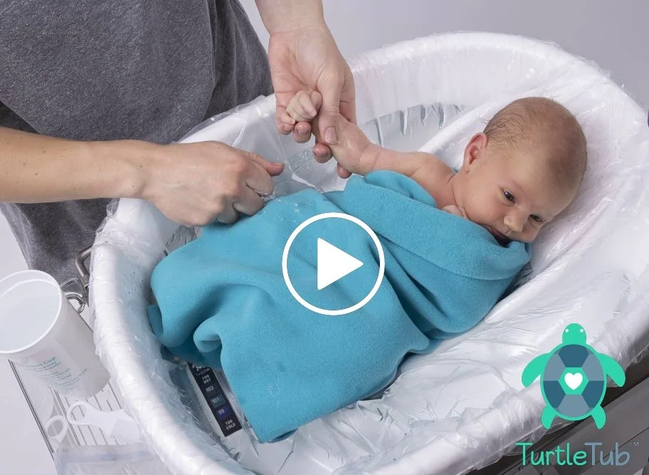 A baby lying in a TurtleTub, swaddled in blue.