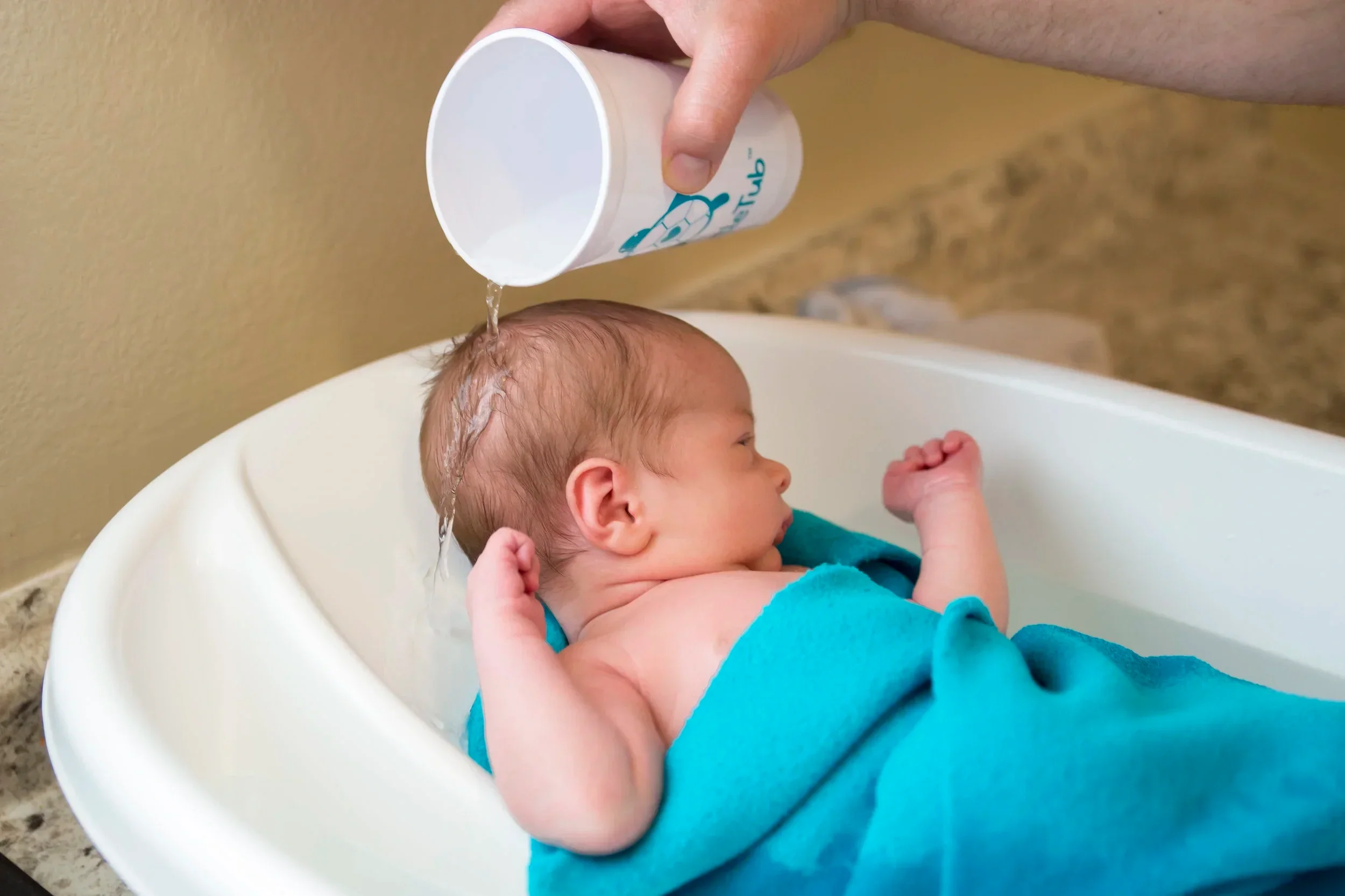Baby in TurtleTub getting a rinse with cup