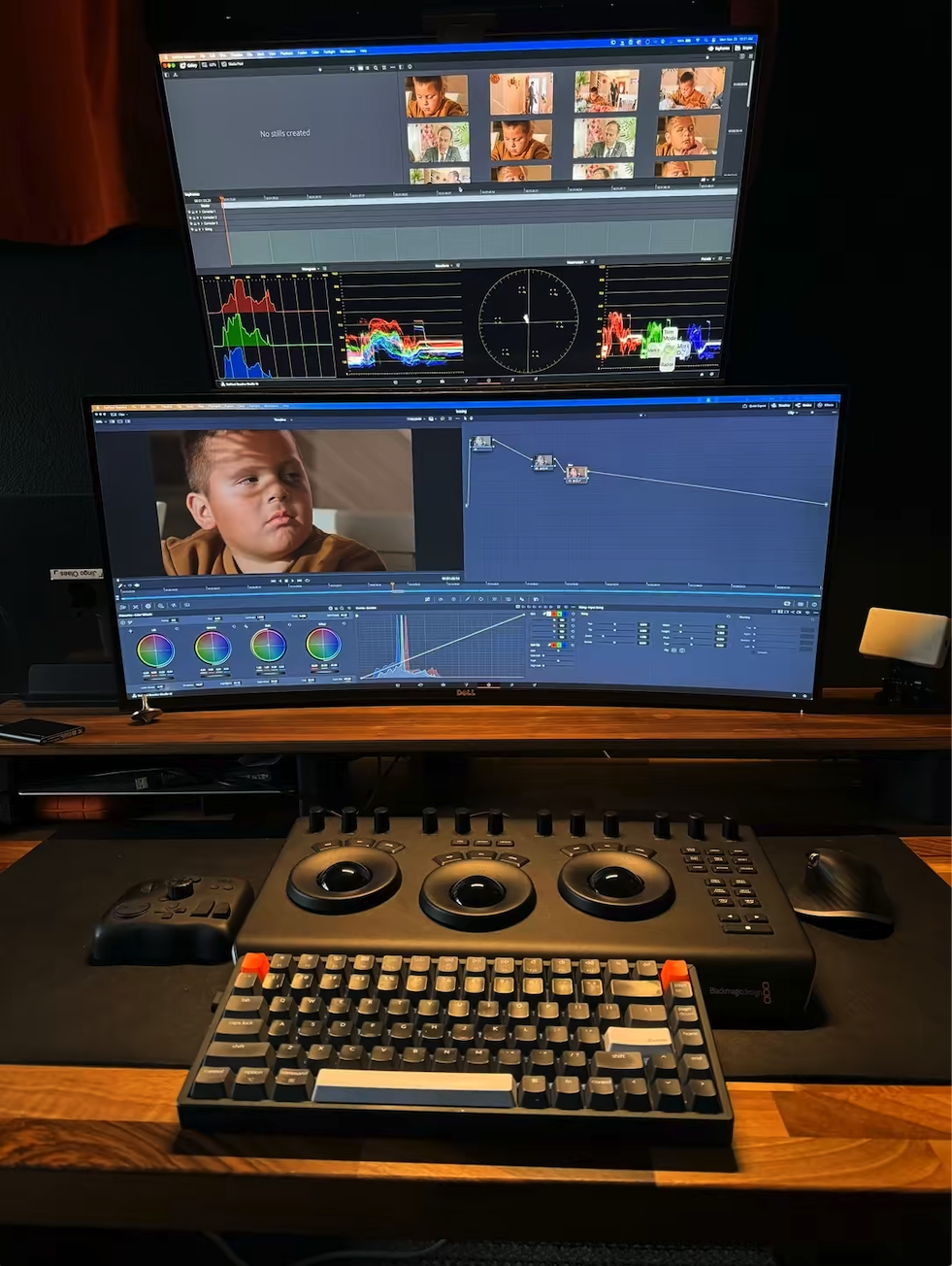 Computer workspace with dual monitors displaying video editing software, keyboard, mouse, control panel, and editing tools, in a dimly lit room.