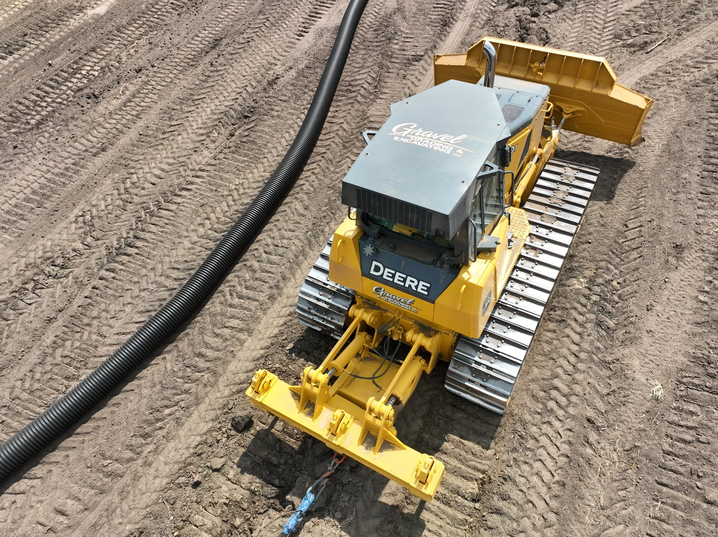 Overhead view of a Gravel Grading & Excavating John Deere track machine pulling corrugated drainage tile through a field in Eastern Iowa