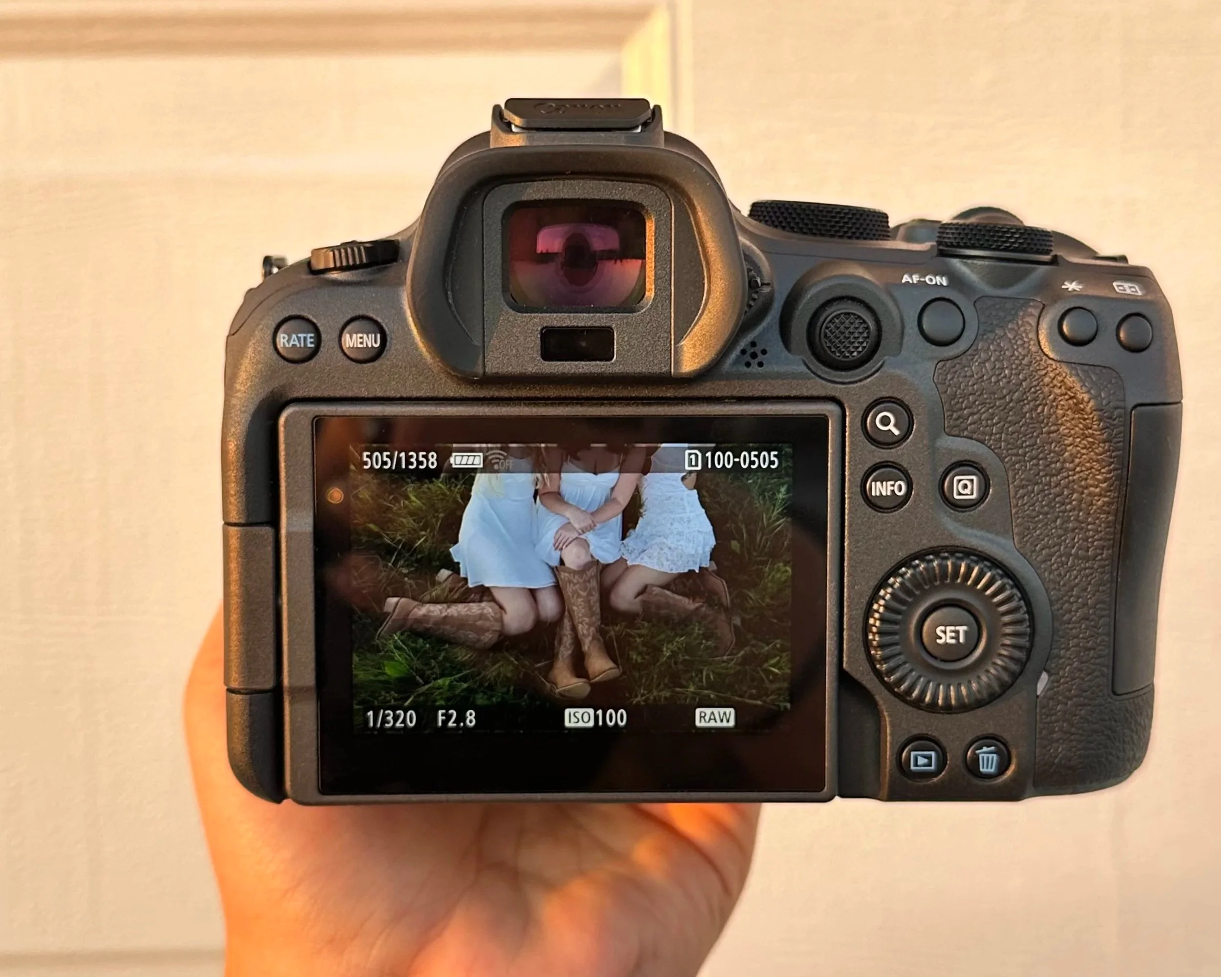 A digital camera displaying a photograph of two women sitting on the grass, one in a white dress and the other in a brown dress, with their arms around each other.