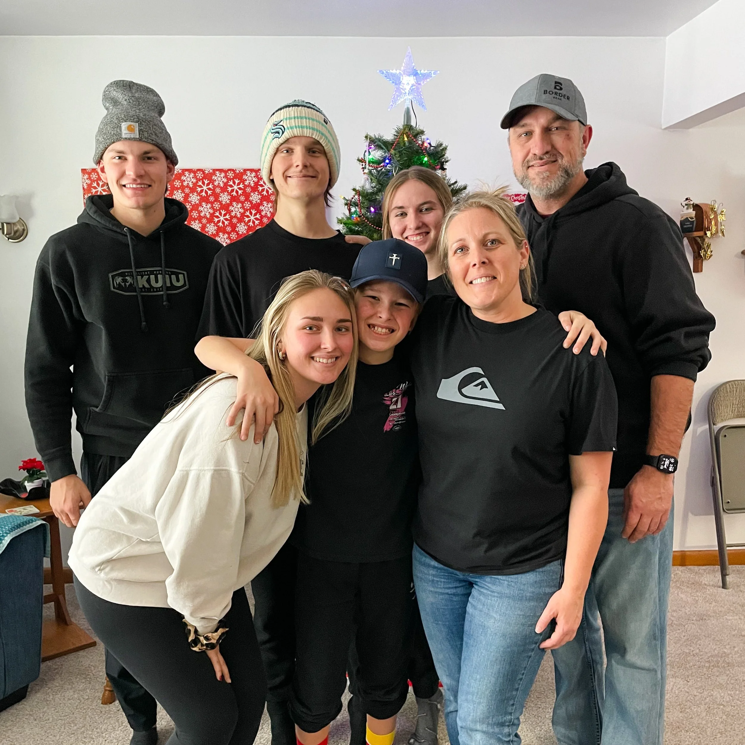 Family group with children and adults posing in front of a decorated Christmas tree inside a home.