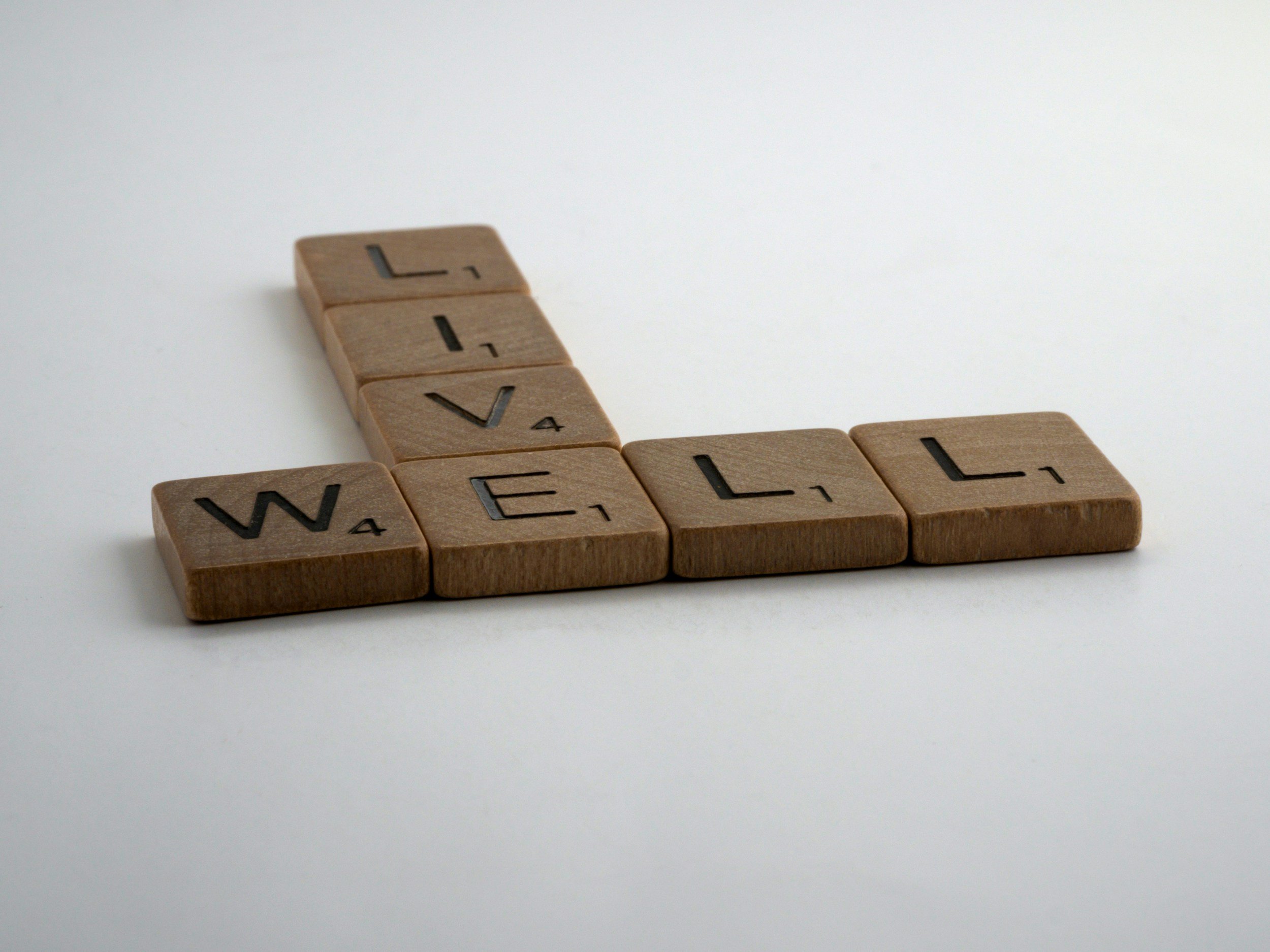 Close-up of wooden Scrabble tiles spelling out the word 'WELL' on a plain white background.