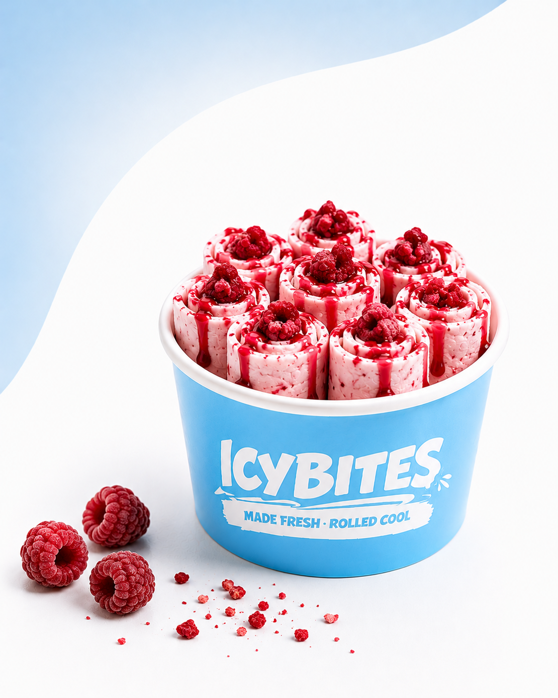 A blue container labeled "Icybites" filled with raspberry-flavored frozen treats topped with fresh raspberries and raspberry sauce, with some raspberries and crumbs on a white surface.