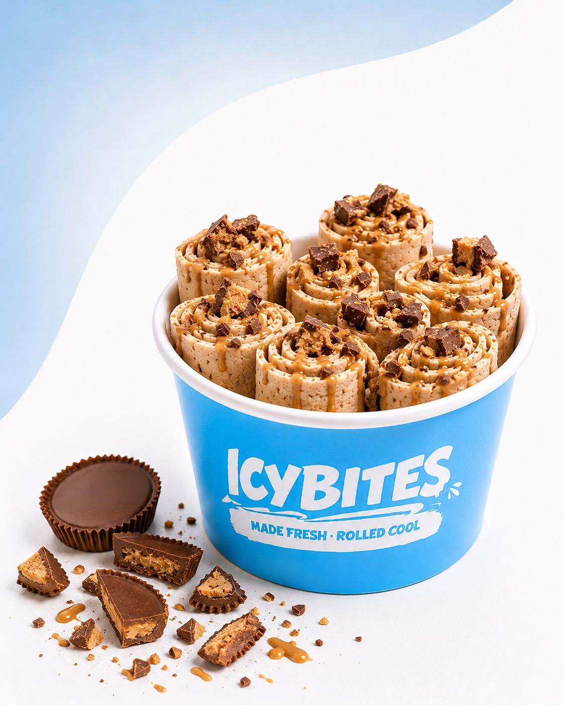 A blue container labeled 'ICY BITES Made Fresh Rolled Cool' filled with caramel and chocolate ice cream bites topped with chocolate chunks. Some broken pieces and chocolate candy are scattered on the white surface outside the container.