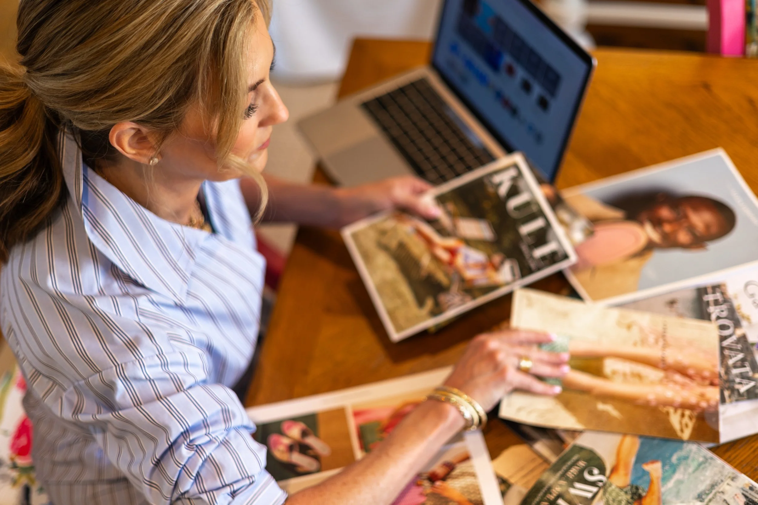 Woman with blonde hair looking at magazines on a wooden table.