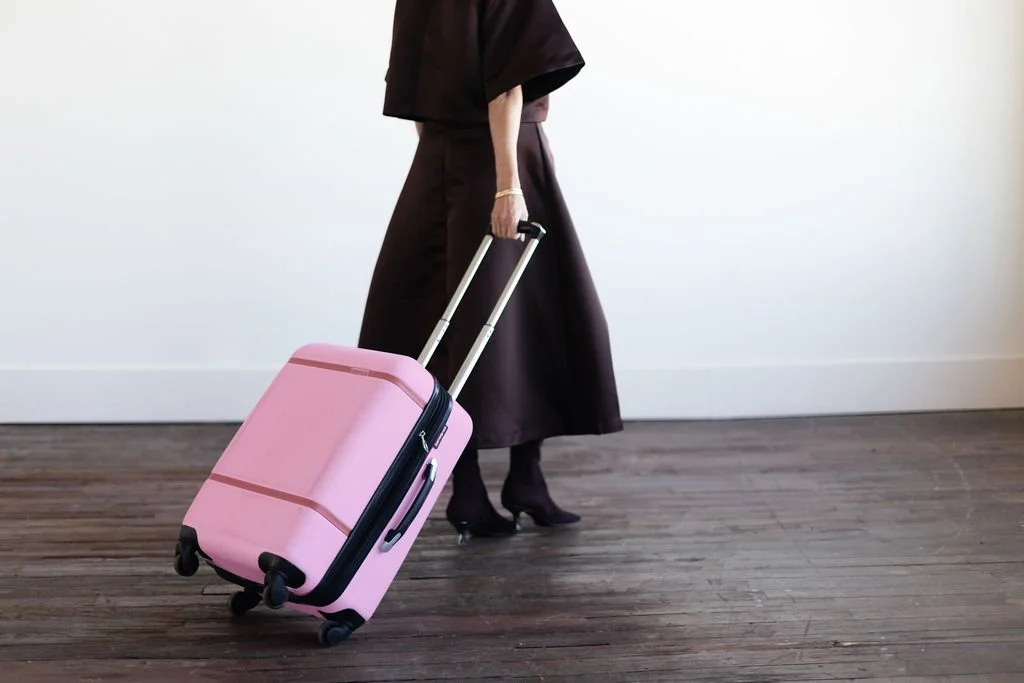 Person walking with a pink rolling suitcase on a wooden floor.