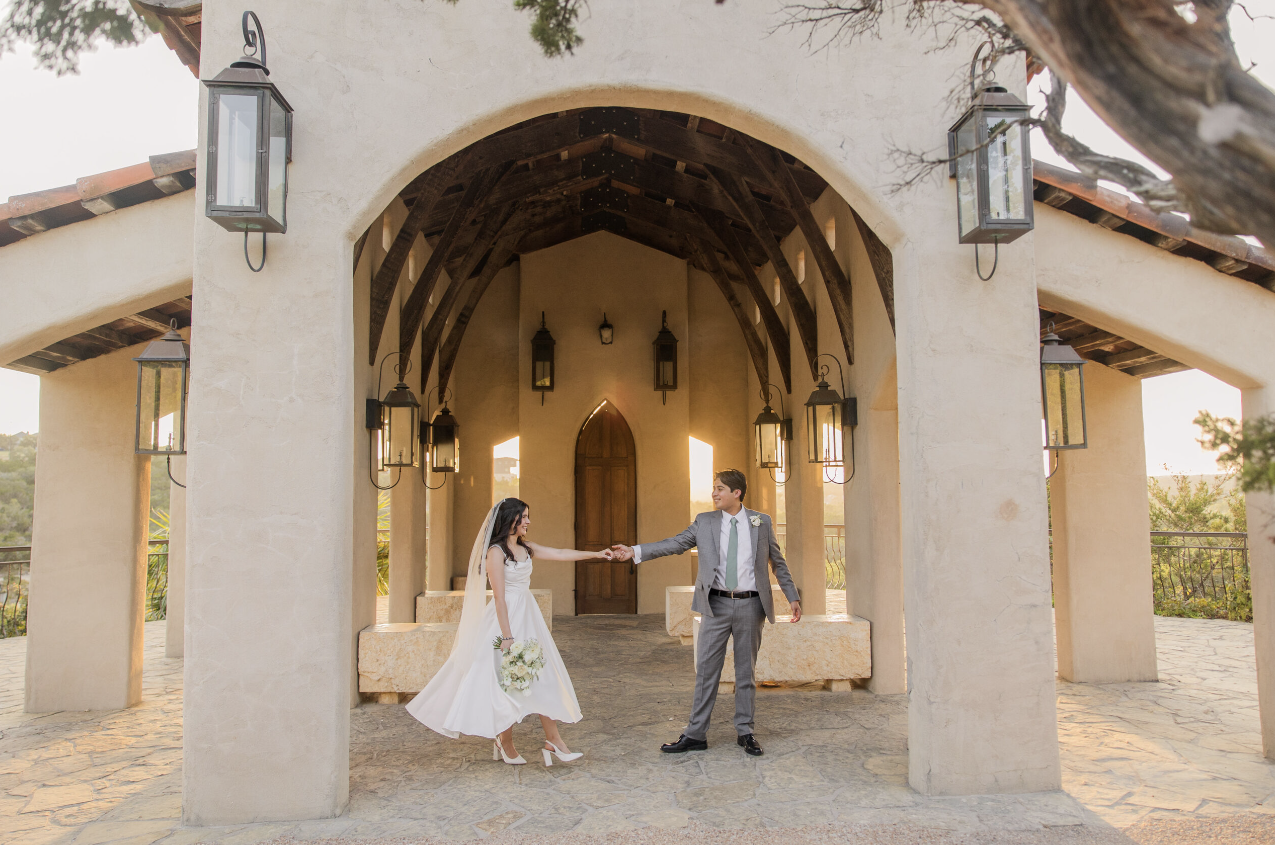 A bride and groom holding hands in a wedding ceremony outside a chapel