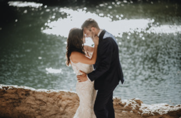 A couple in wedding attire sharing an intimate moment by a body of water.