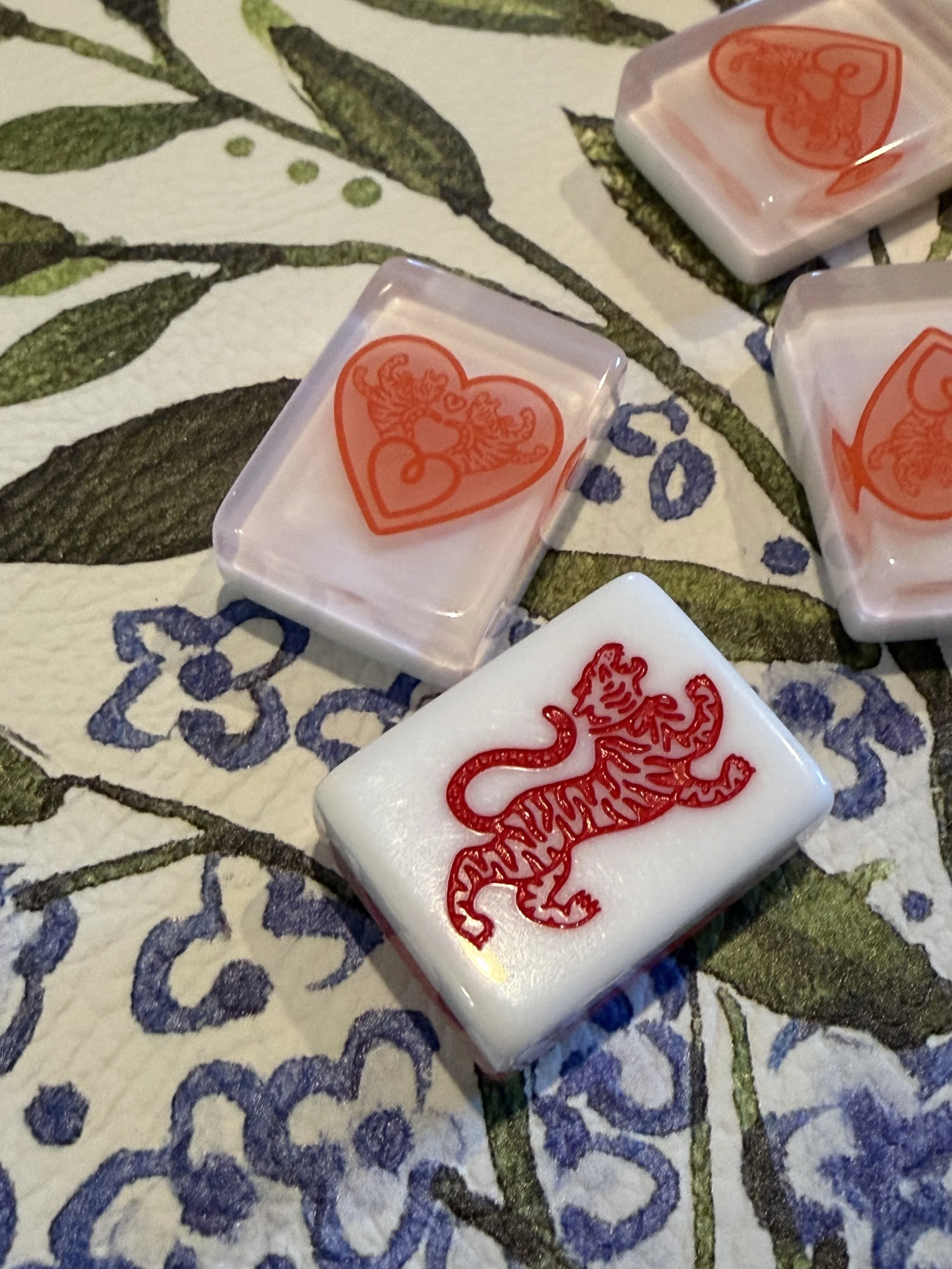 Decorative tiles, one featuring a red lion and another with a red heart containing a dragon, placed on a floral-patterned surface.