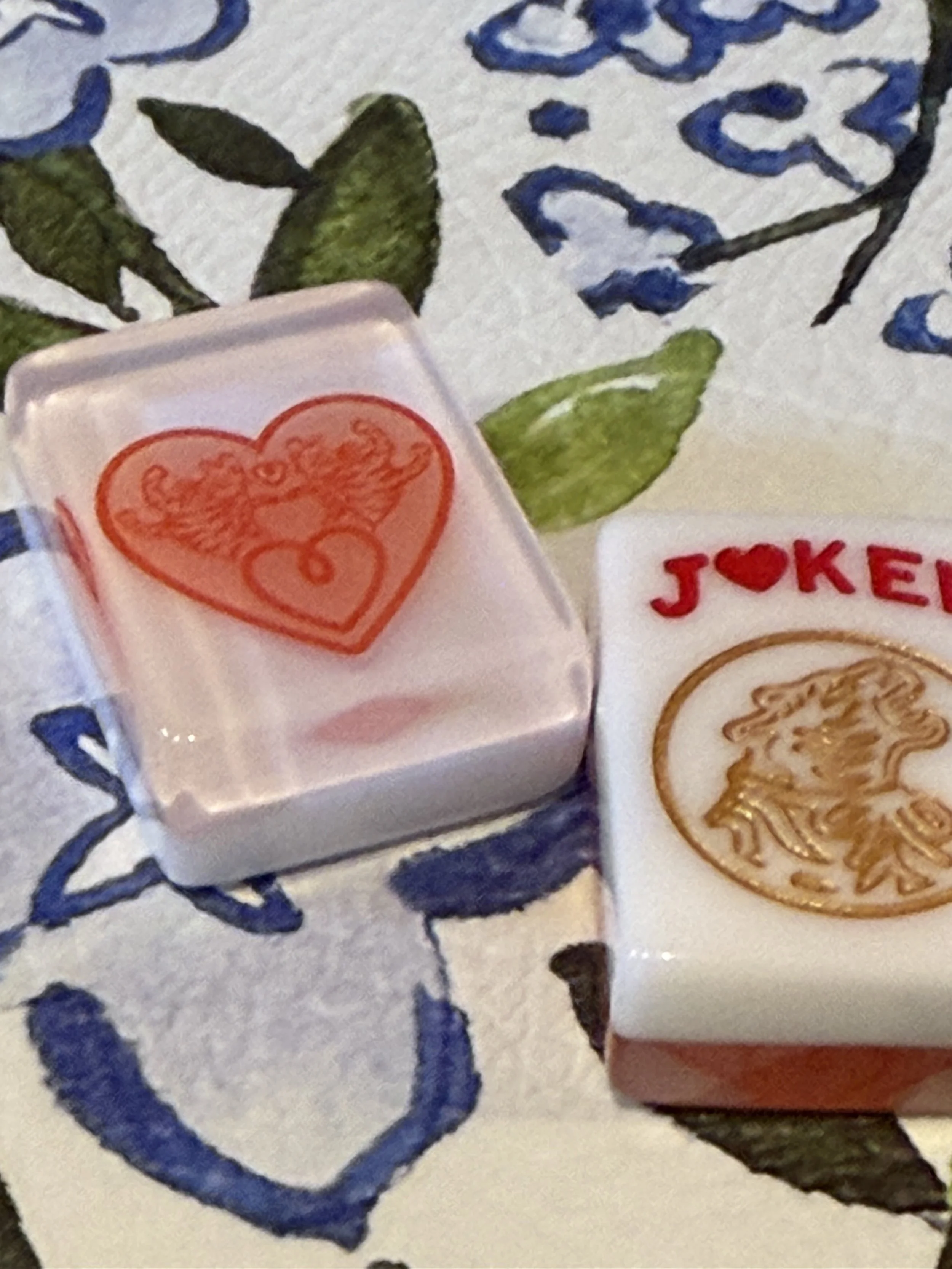 Close-up of decorative tiles featuring a red heart with a crown, smiley face outline, and the word 'JOKER' with a red heart replacing the 'O'.