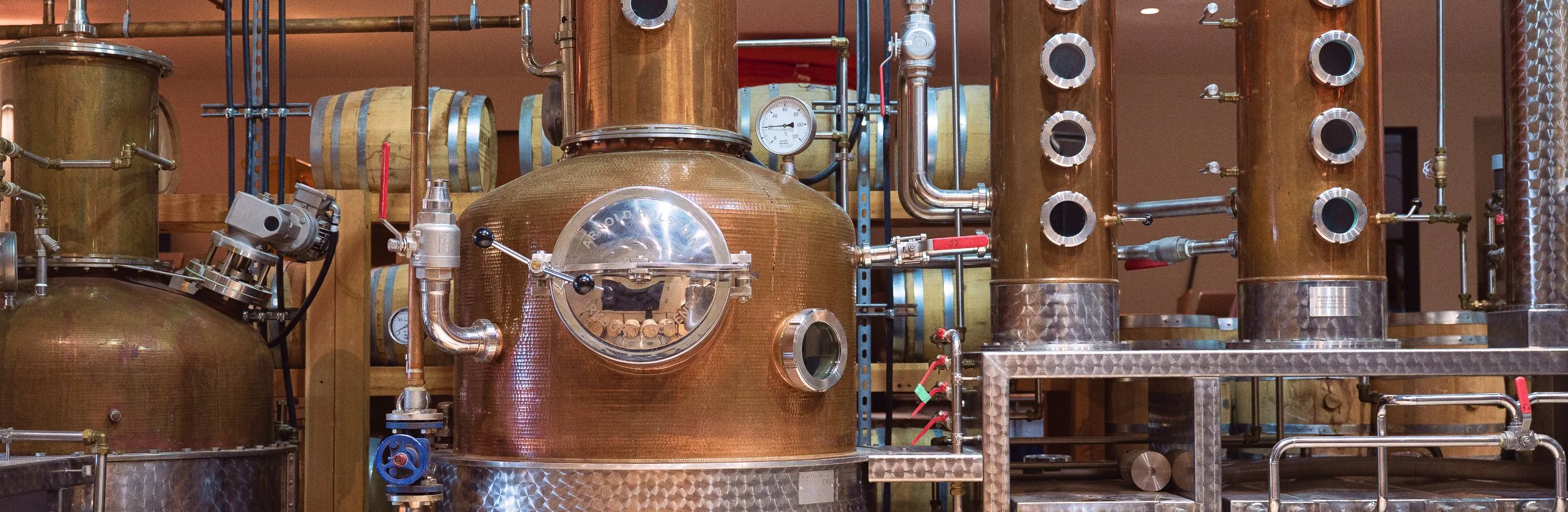 Copper distillation equipment with pipes, gauges, and valves in a distillery.