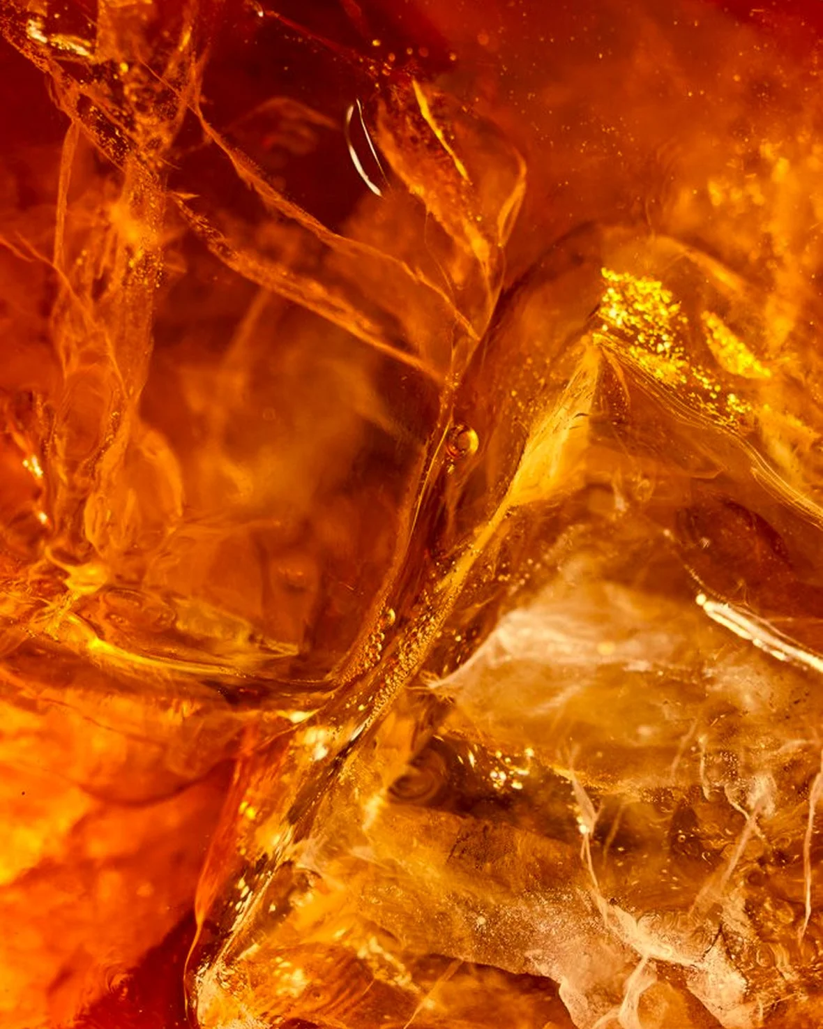 Close-up of ice cubes in amber whisky, showing intricate textures and reflections.