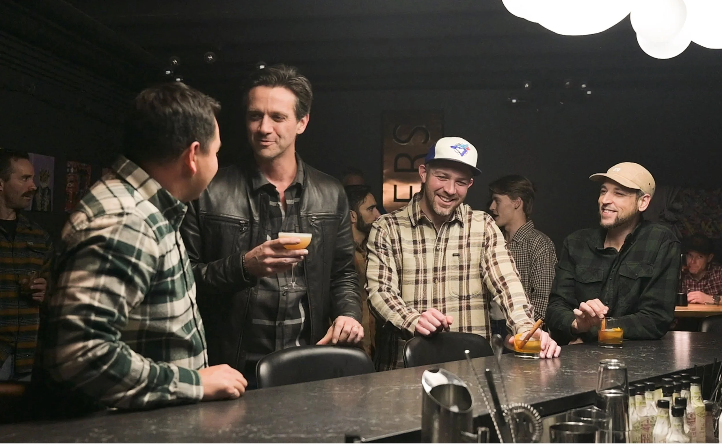 A group of men socializing in Shakers Speakeasy, holding drinks, talking, and smiling.
