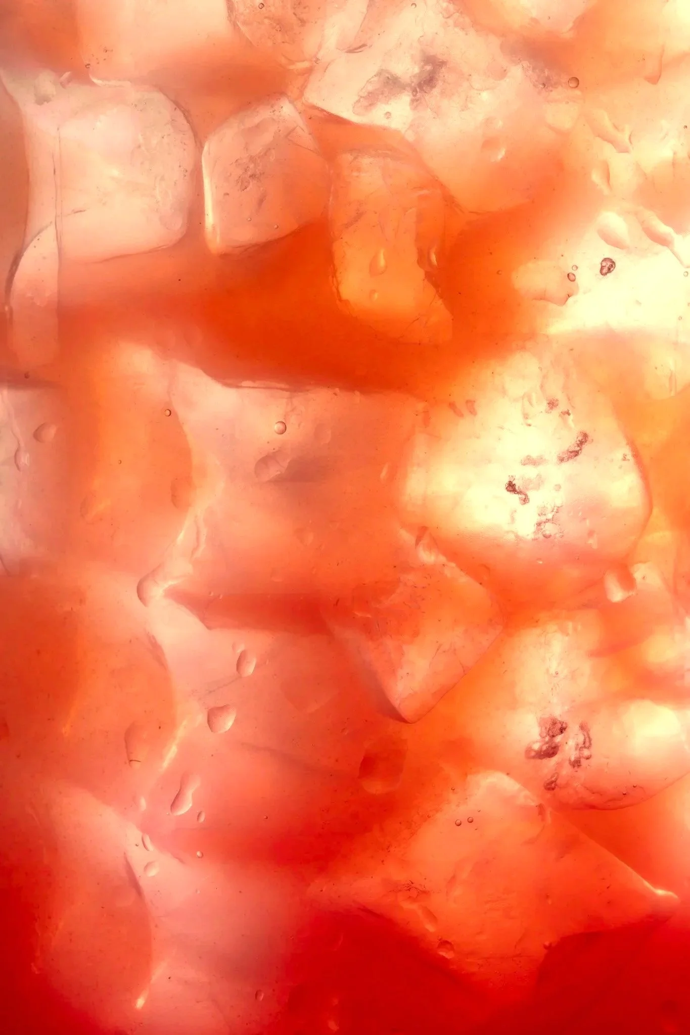 Close-up of ice cubes in orange ombre cocktail with water droplets on the surface.