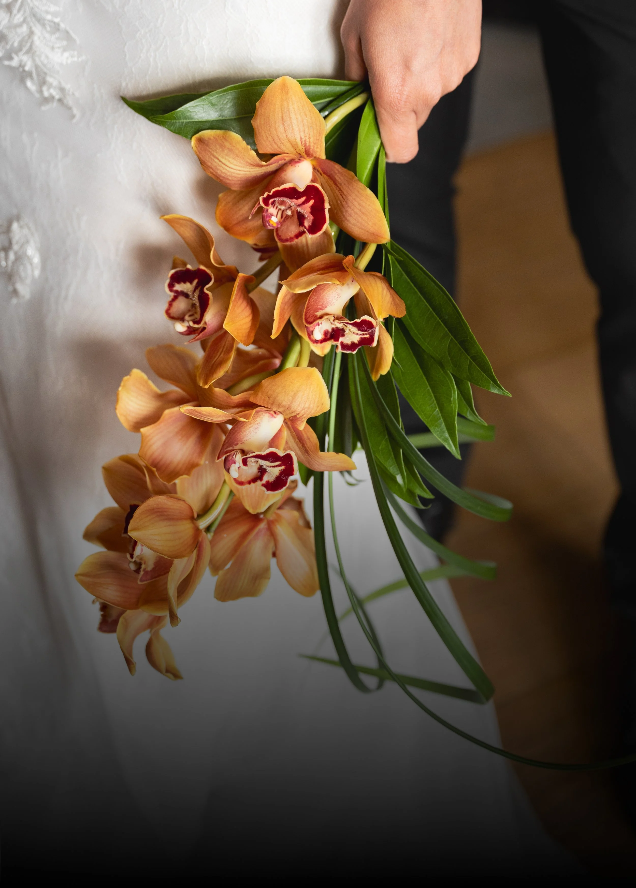 A bride holding a bouquet of orange orchids with green leaves.