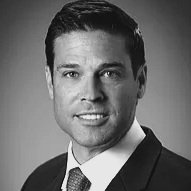 Black and white headshot of a smiling man wearing a suit and tie