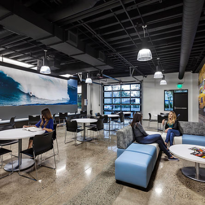 Modern cafe with tables, chairs, and a blue mural of a wave on the wall. Several people are sitting and chatting.