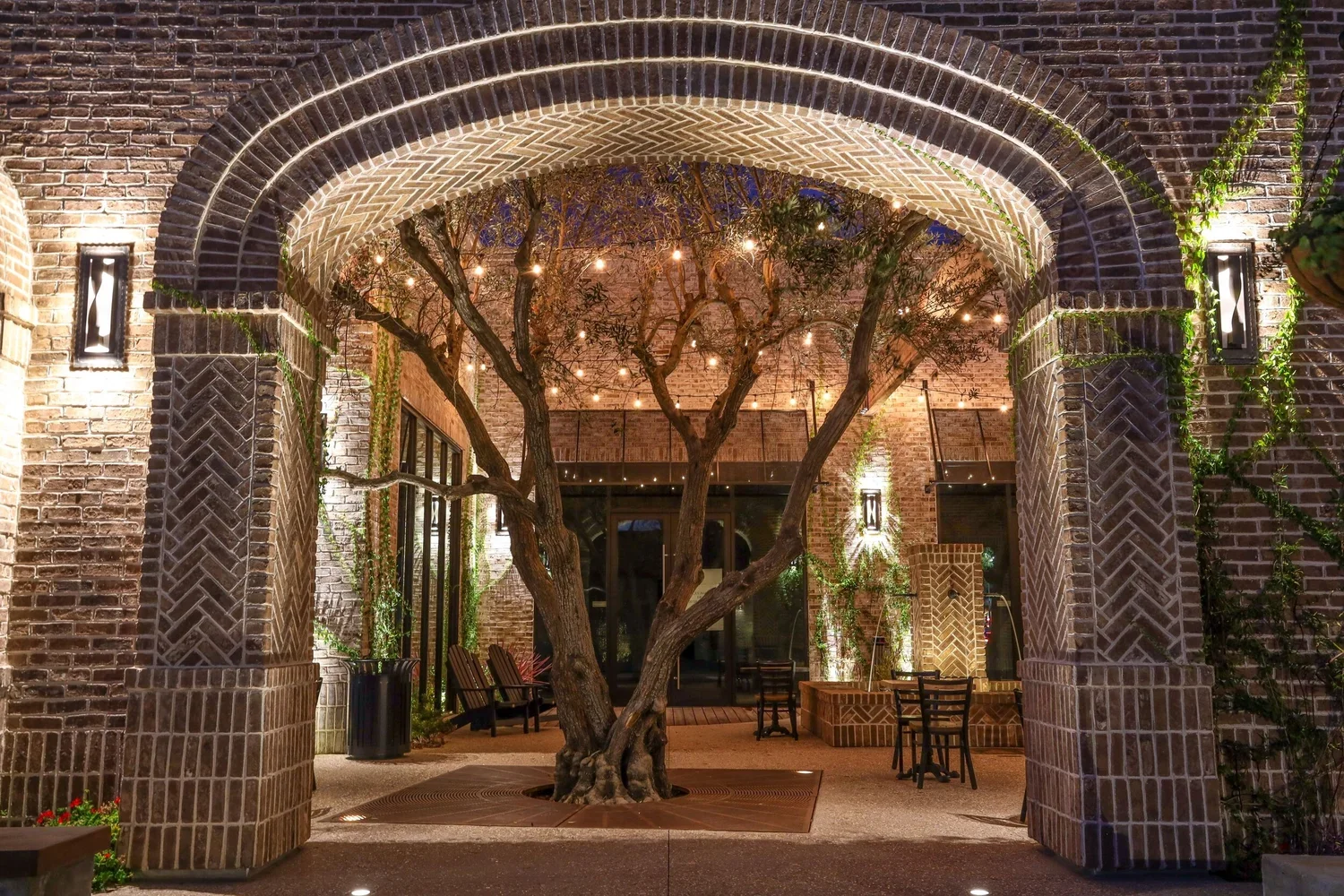 Indoor patio with brick archway, trees, string lights, and outdoor furniture.