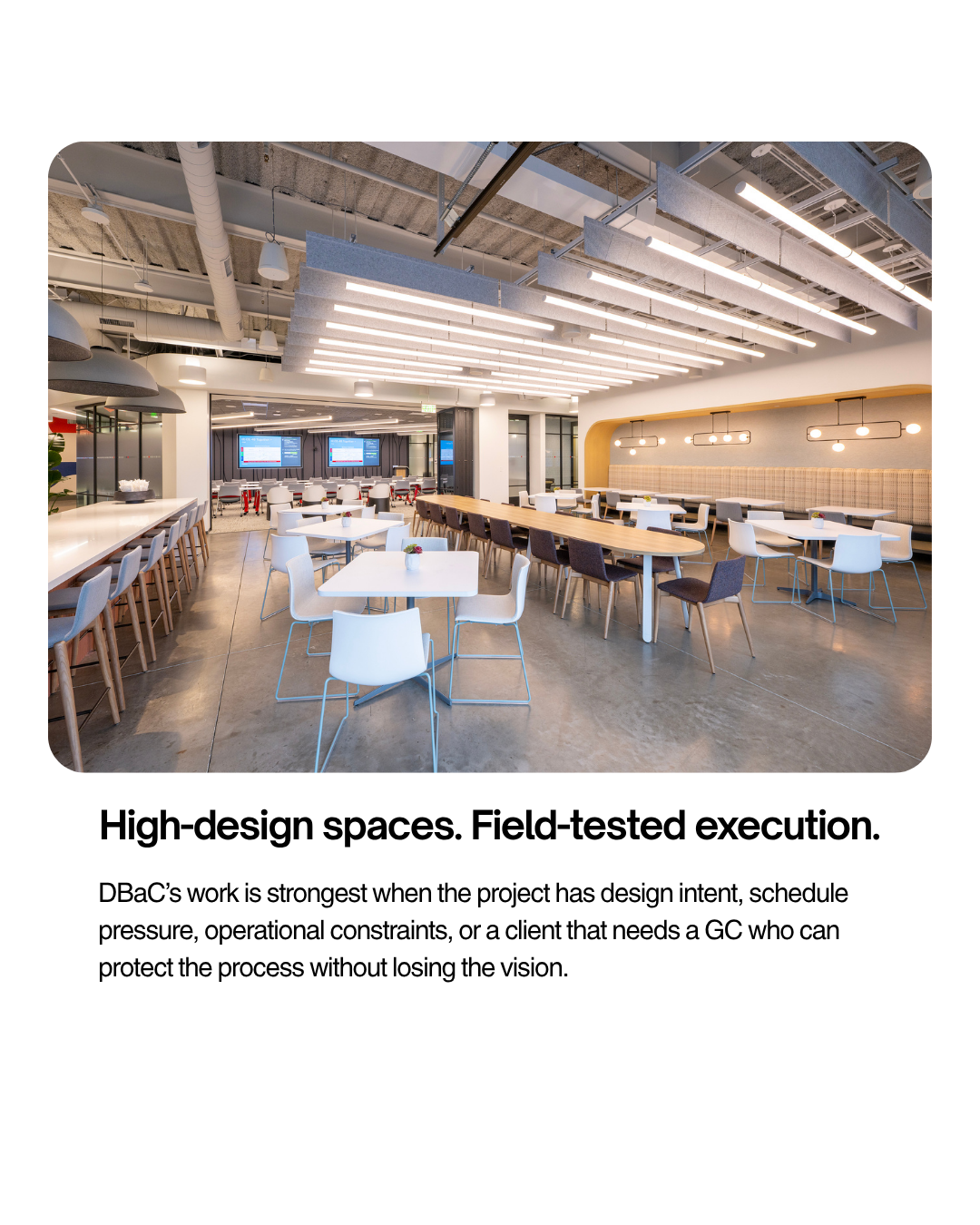 Modern open-plan office or cafeteria with various seating arrangements, including tables with chairs, pendant lighting, and digital screens on the wall.