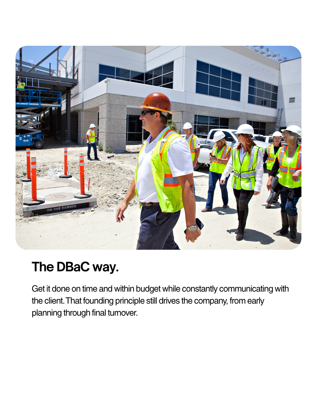 Construction workers in reflective vests and hard hats walking outside a building site on a sunny day.