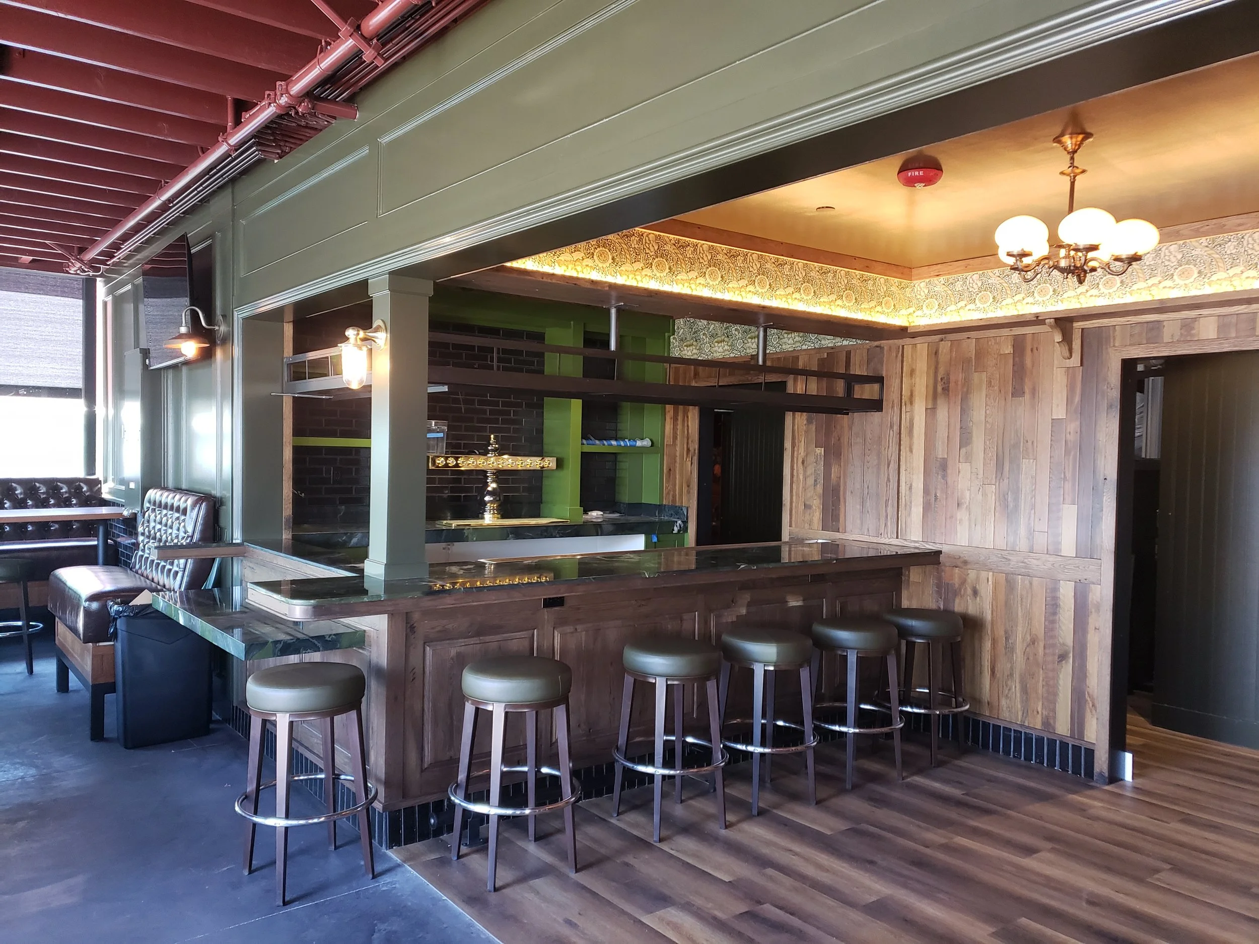 Interior of a modern restaurant or bar with a wooden bar counter, bar stools, and decorative lighting fixtures on the ceiling.