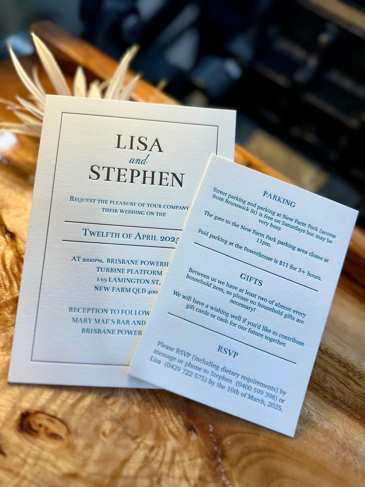 Wedding invitation with details about the date, time, and location, alongside additional information about parking, gifts, and RSVP. The invitation is on a wooden surface with a decorative element in the background.