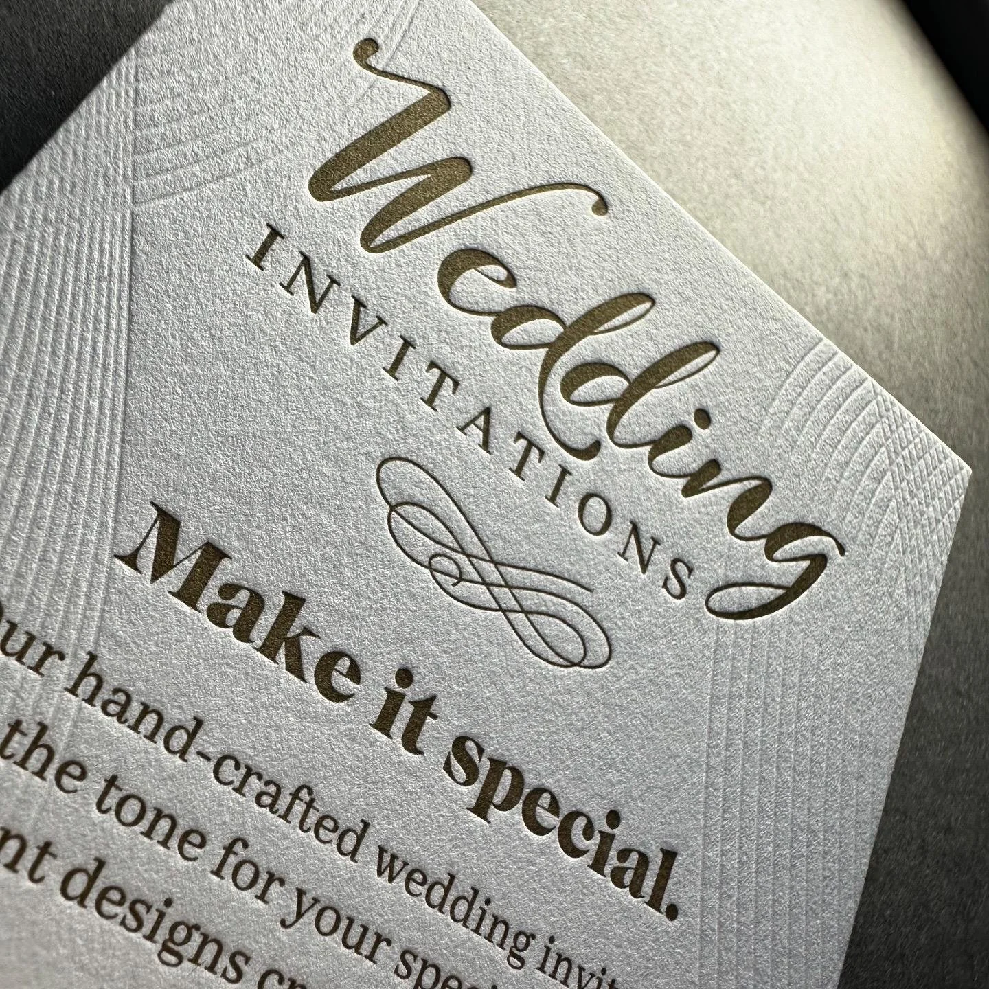 Close-up of a wedding invitation with embossed gold and black text, featuring elegant calligraphy and decorative elements.