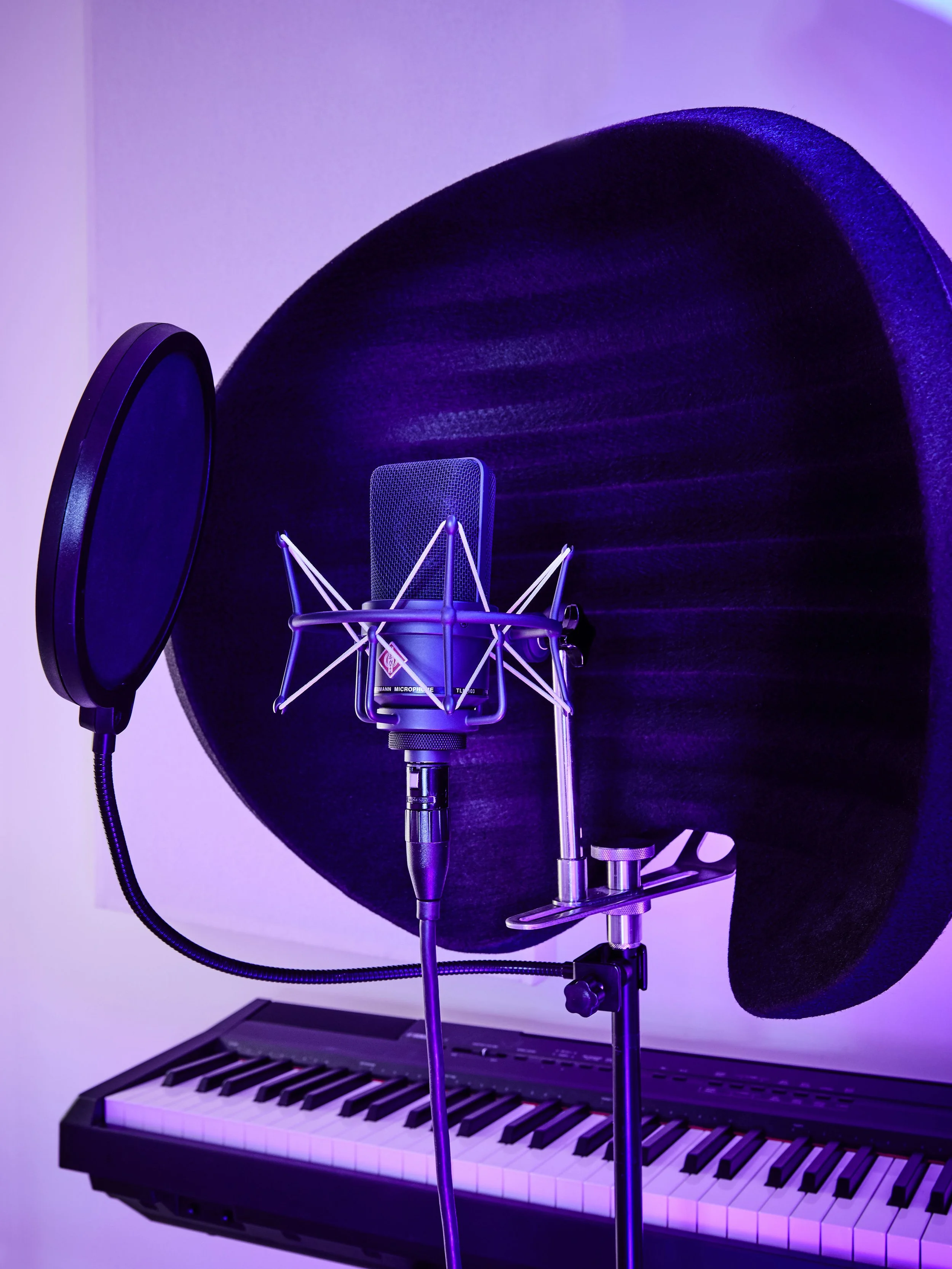 Music recording setup including a microphone on a stand with a pop filter, a pair of headphones, a keyboard musical instrument, and a purple-lit background.