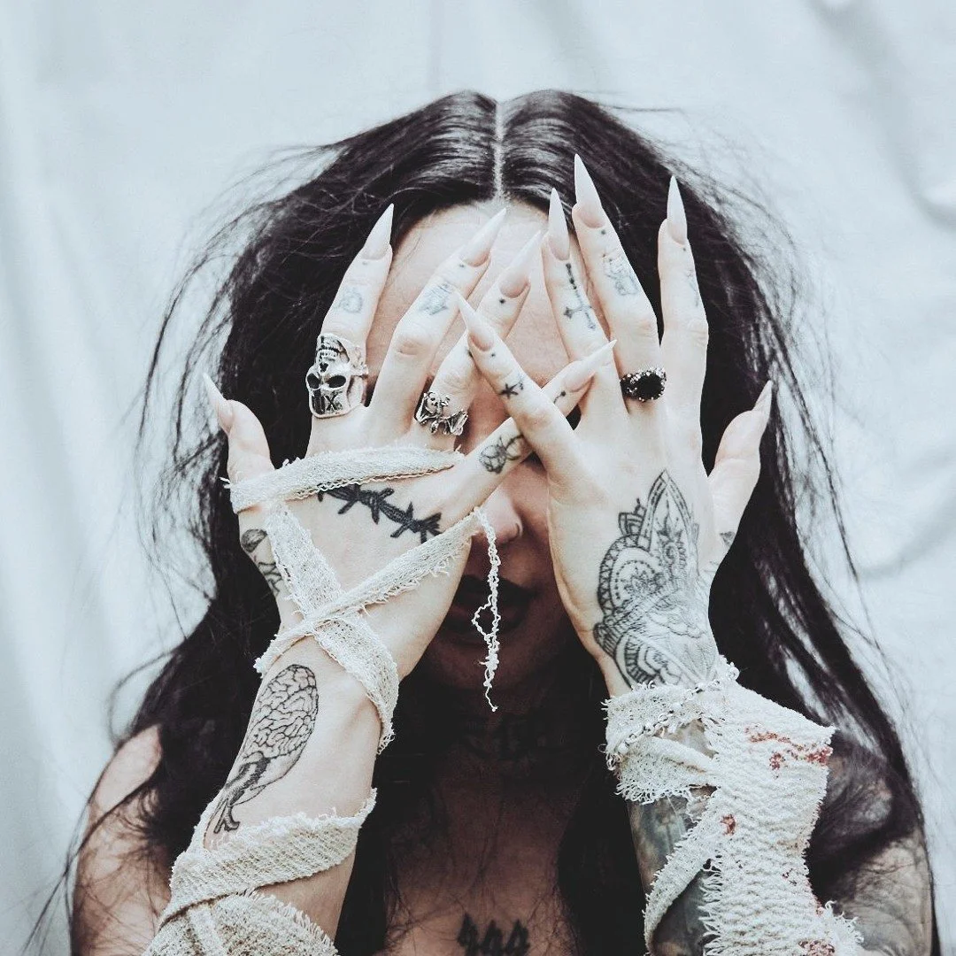 Ronavella, Owner of Haven Studios London. Covering her face with her hands, wearing rings, bandages & tattoos