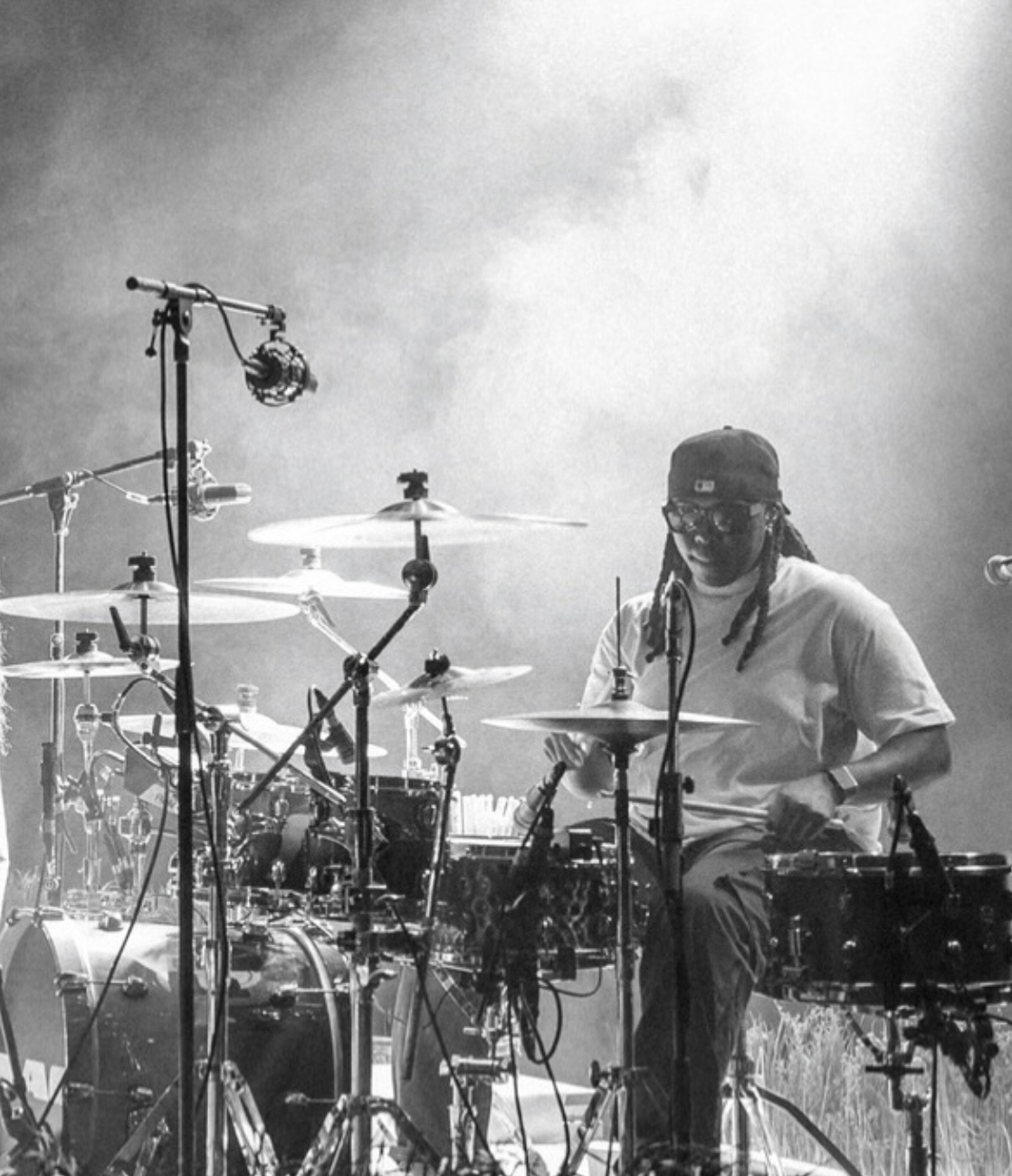 A person playing a drum set on stage, with microphones and stage lights visible.