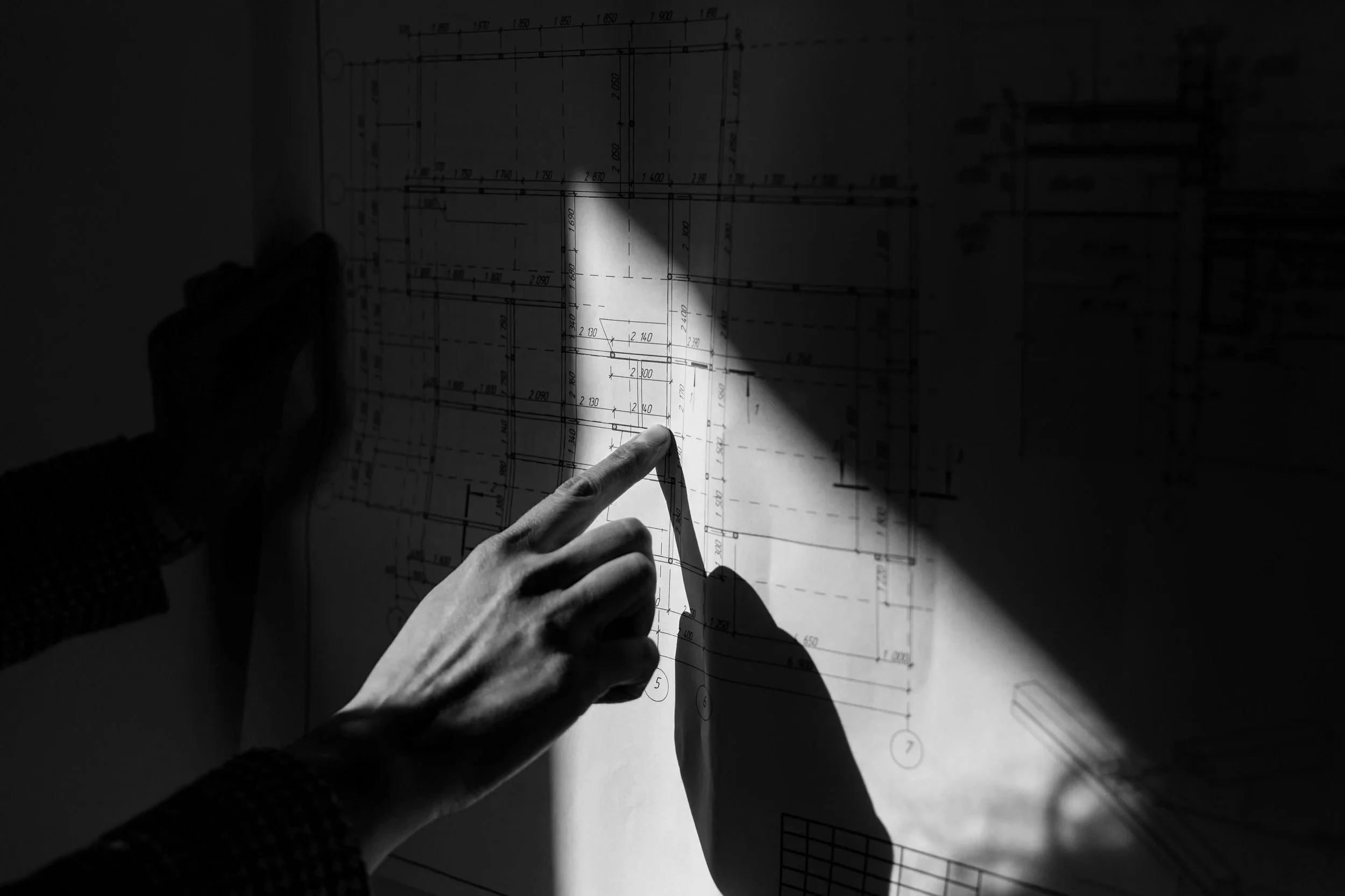 Hand pointing at a detailed architectural floor plan in dramatic light — hospitality design review and advisory services.