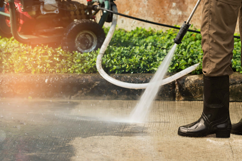 Person using a power washer to clean a concrete surface outdoors.