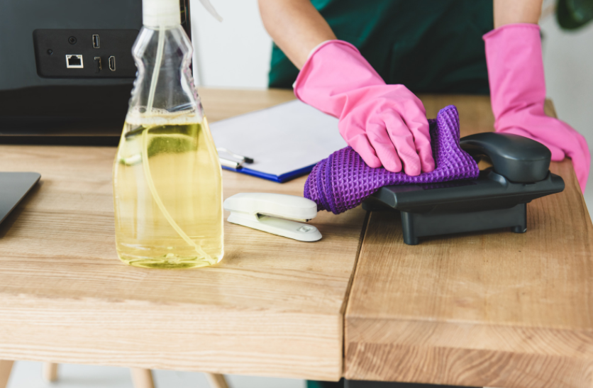 a cleaner cleaning an office desk. Wiping down a phone and high touch points.