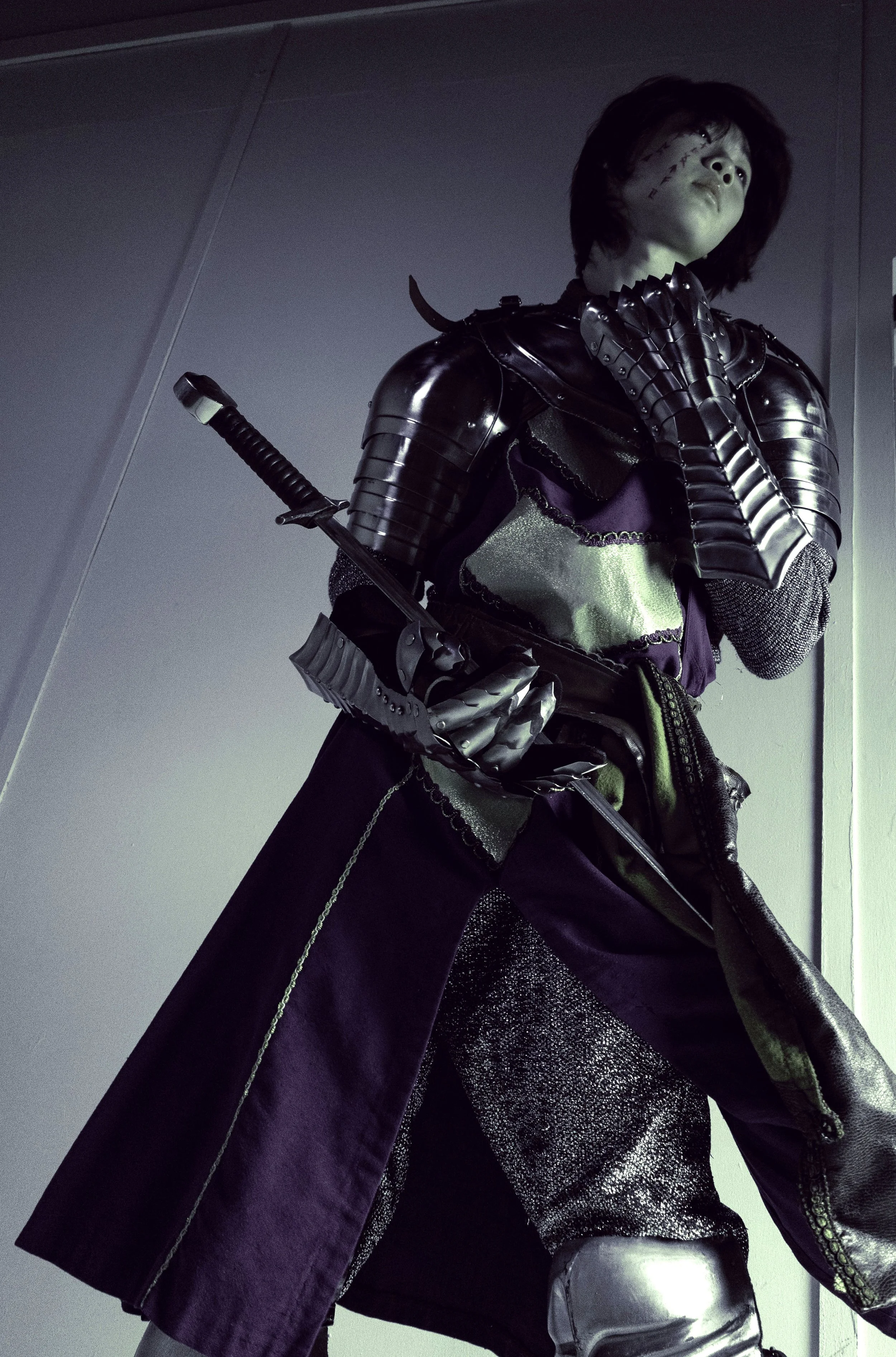 A female figure dressed in futuristic armor, with a metallic sword strapped to her back, wearing a purple cloak, silver and black clothing, and a silver metallic glove.