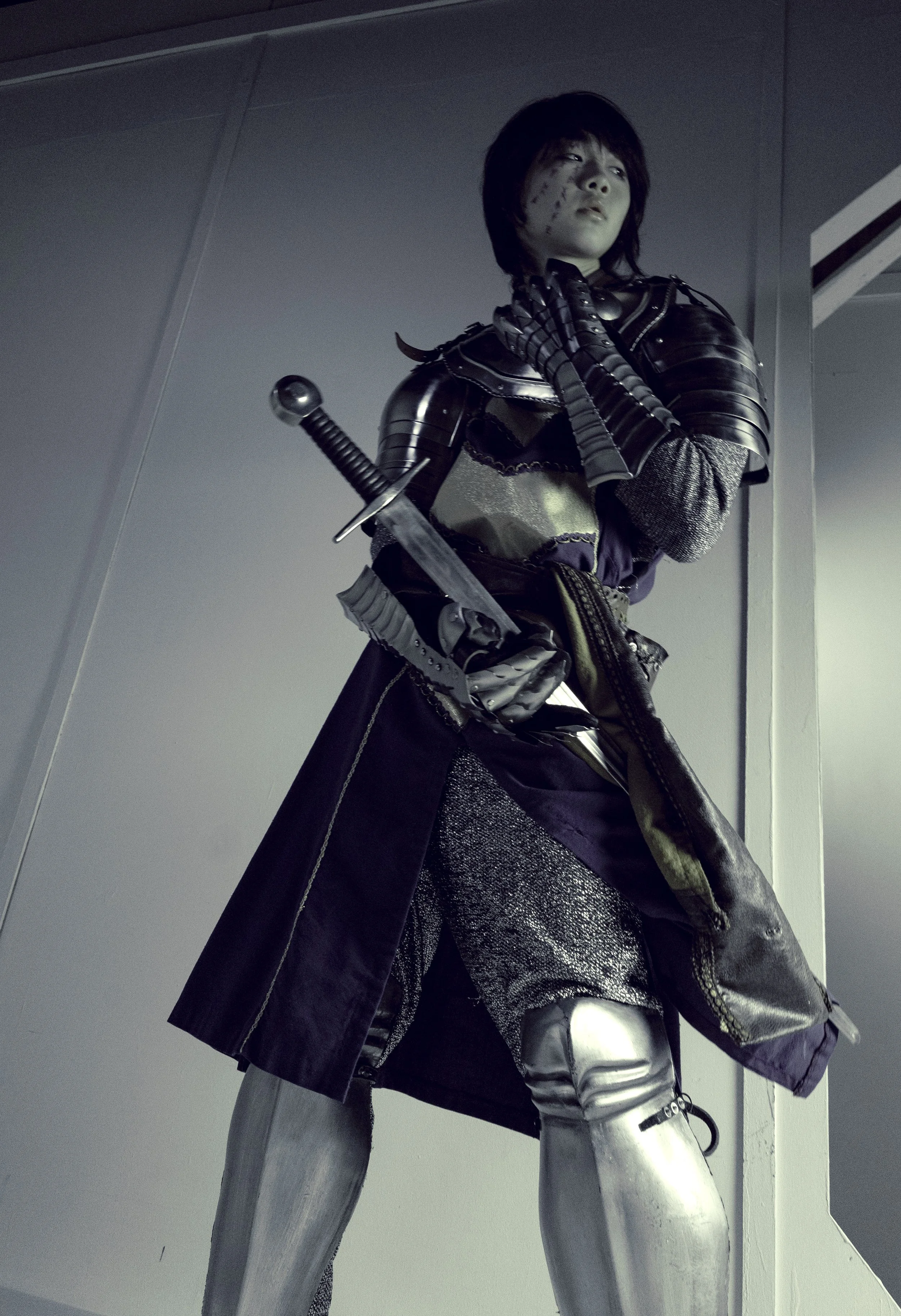 A person dressed in medieval armor holding a sword, standing with legs apart in an indoor setting.