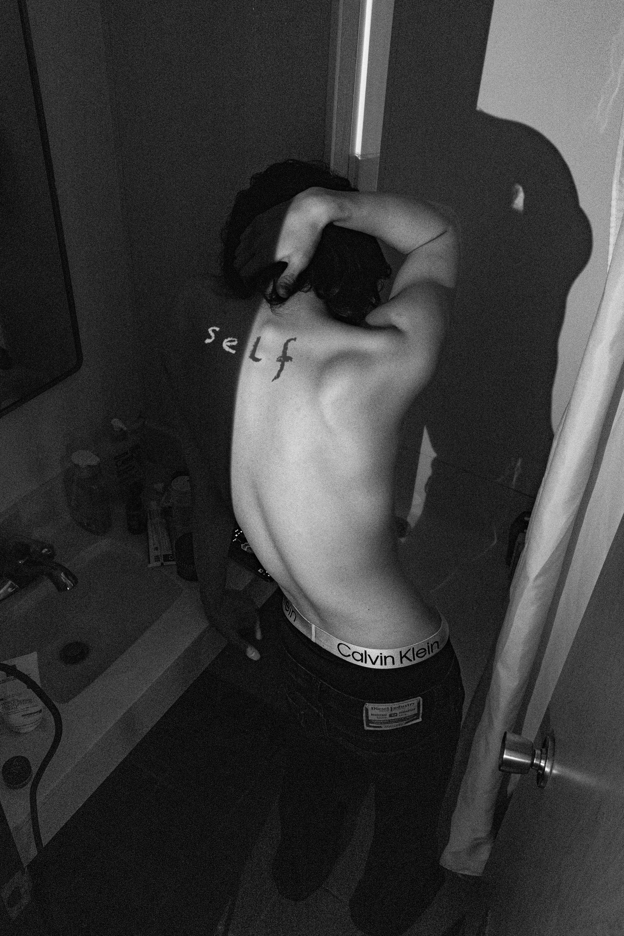 A person taking a mirror selfie in their underwear, with the word 'self' written on their back.