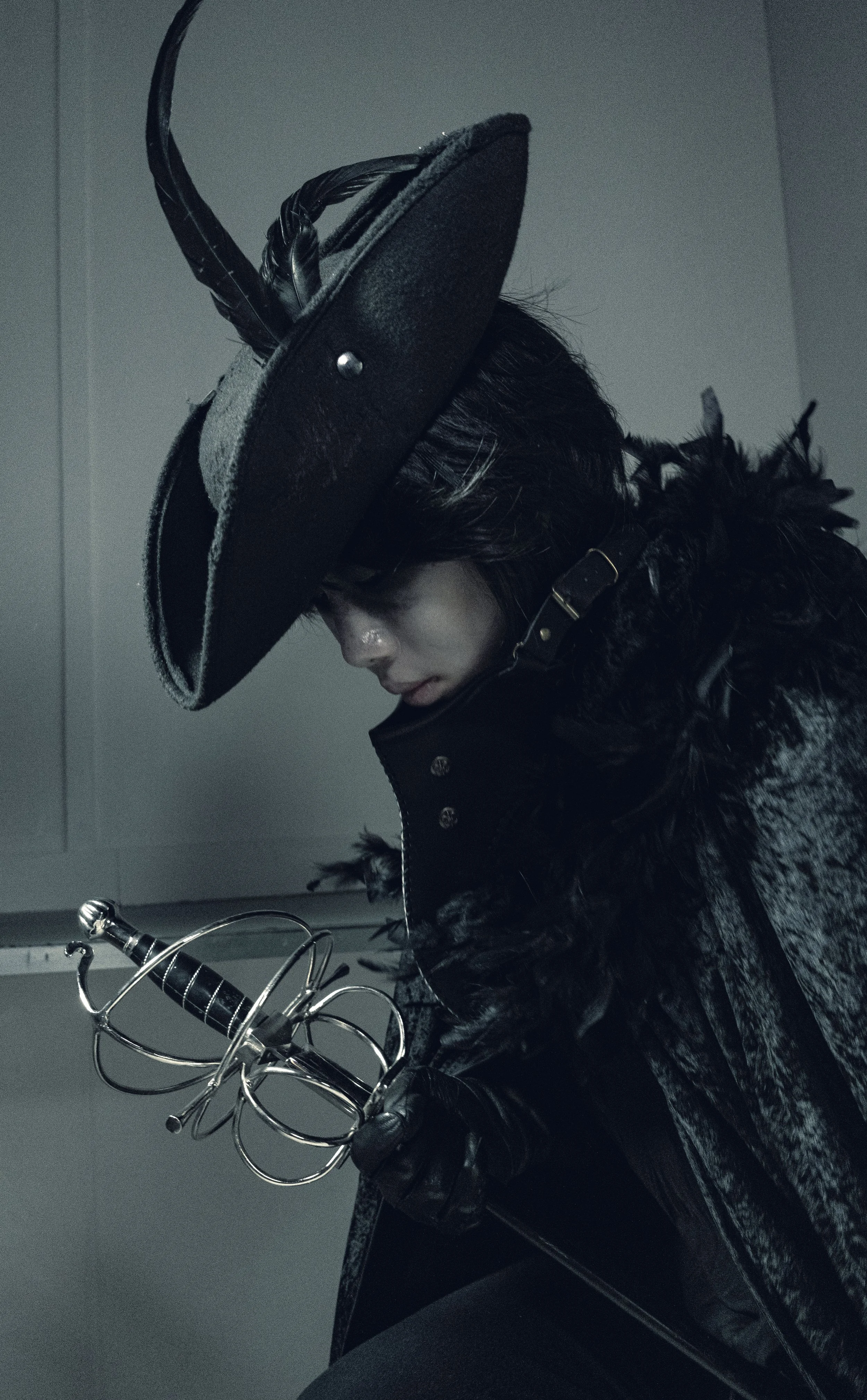 Person wearing a large black hat with feathers, a black feathered coat, and black gloves, holding a silver sword.