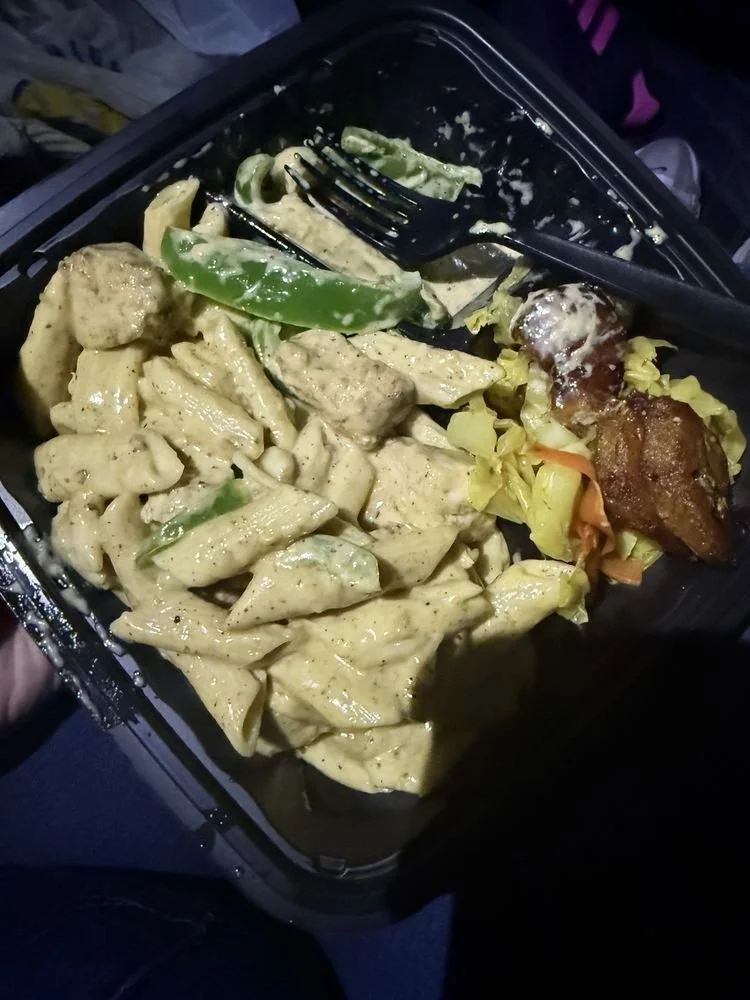 Takeout container with creamy pasta, green bell pepper slices, roasted chicken, and cooked vegetables.