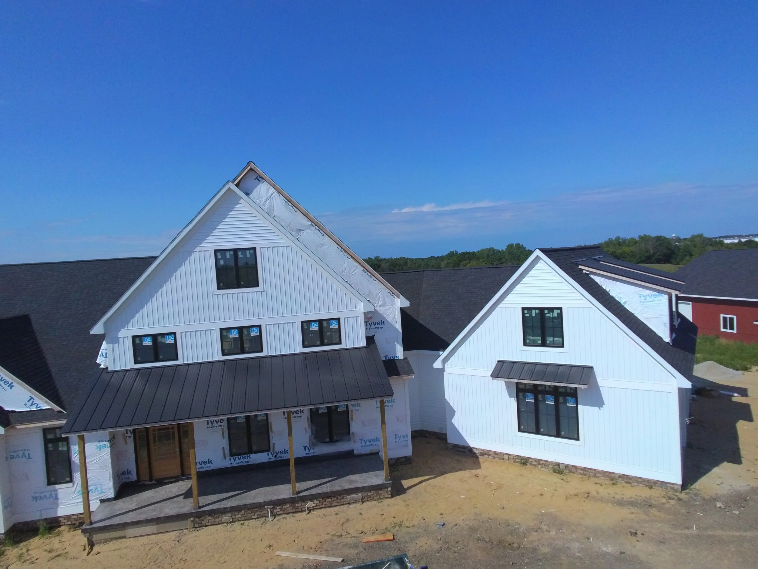 Construction site with partly built white houses with black roofs, some windows installed, and construction materials visible, under a bright blue sky.