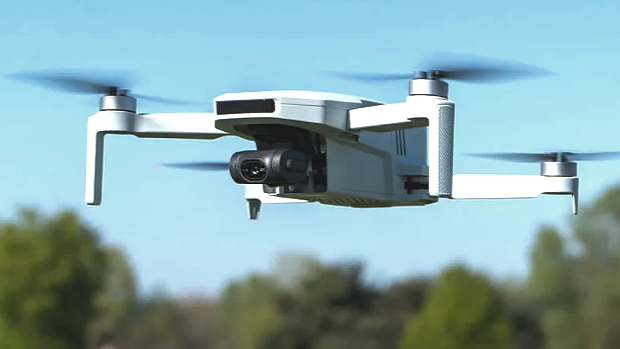 White quadcopter drone flying in the sky with trees below