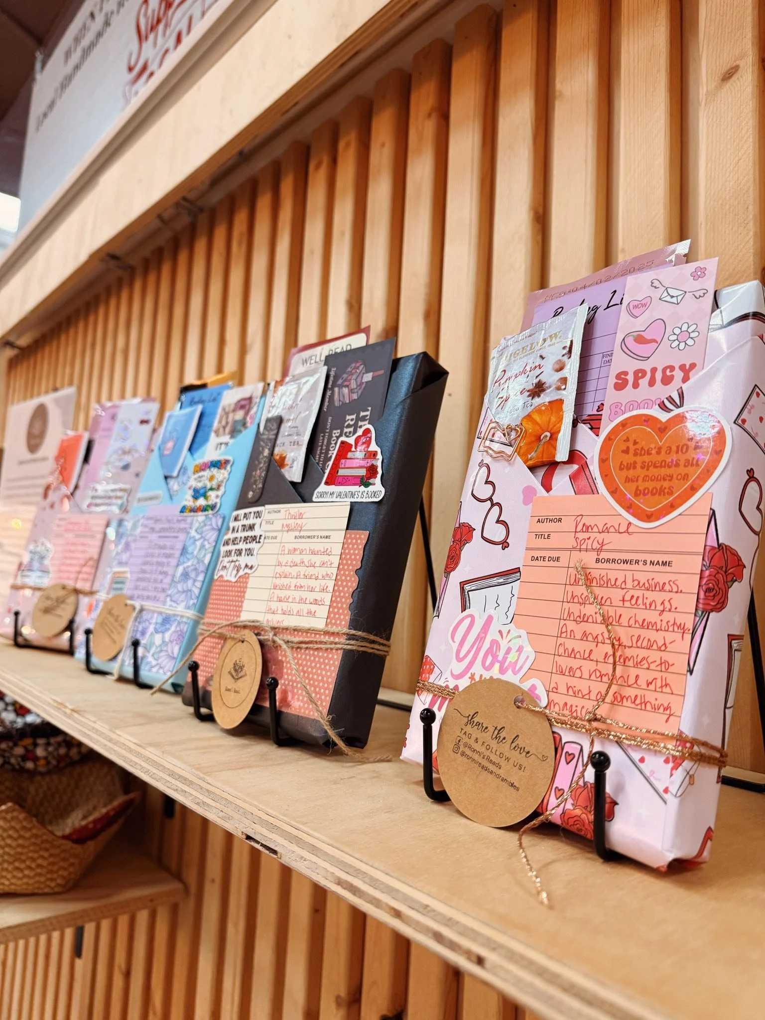 Valentine's Day cards displayed on a wooden shelf, decorated with ribbons and tags, for sale or gift-giving.