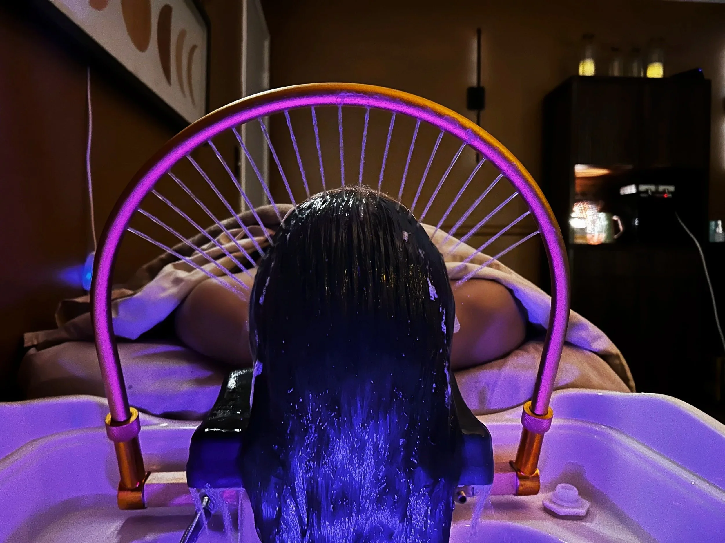halo waterfall falls on woman who is laying down in a relaxing spa room.