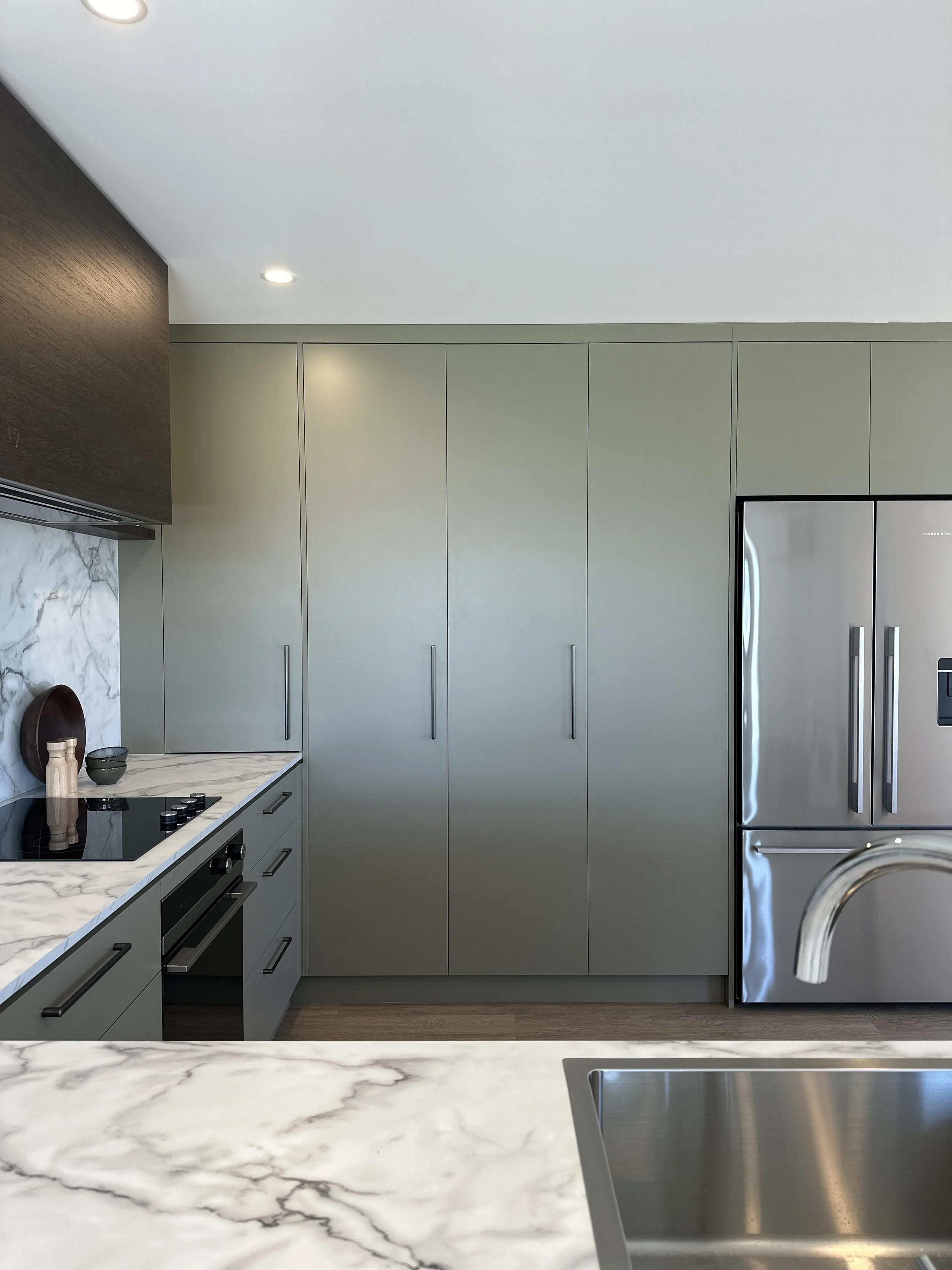Modern kitchen with white marble countertop, sleek beige cabinets, stainless steel refrigerator, and a copper sink.