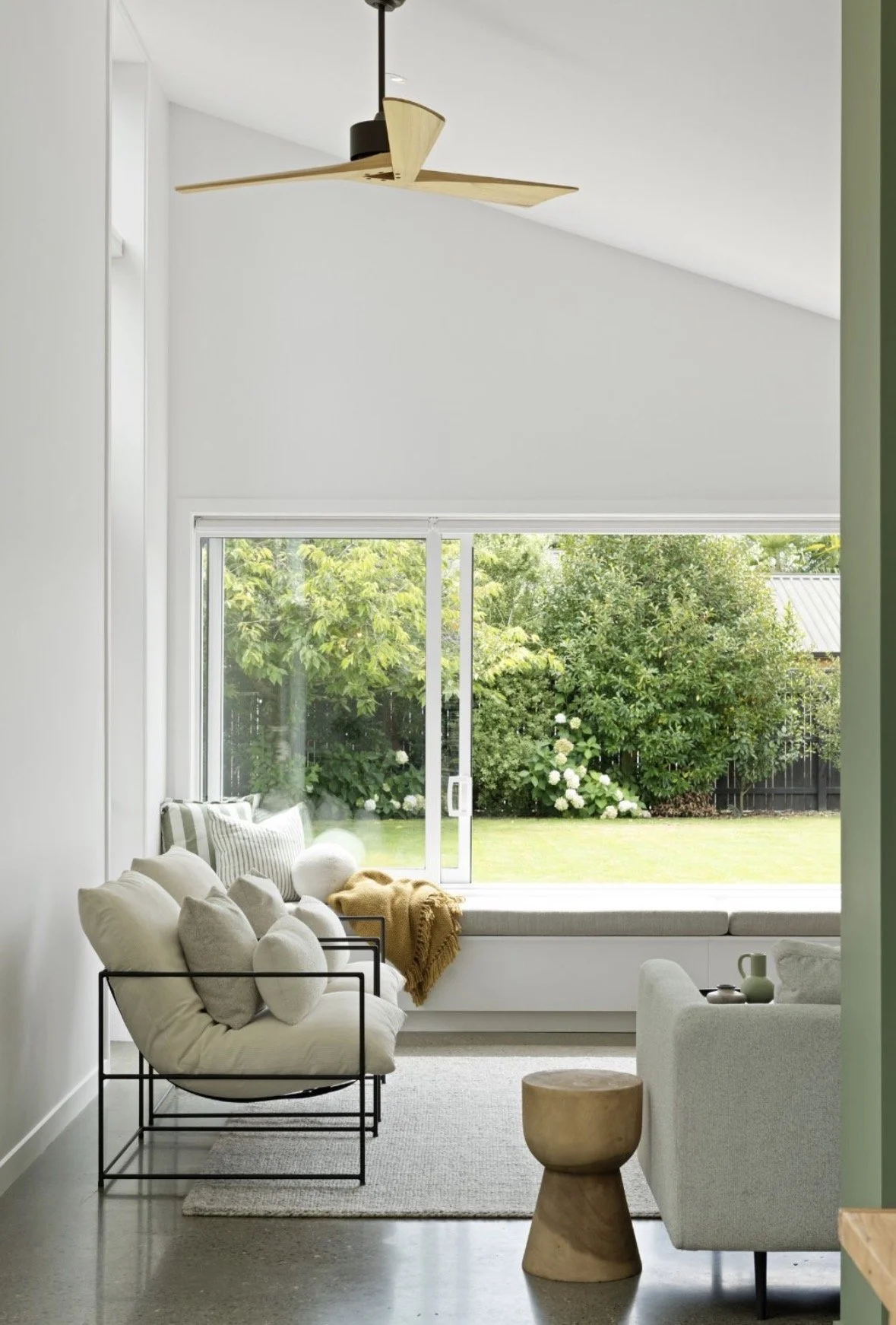 Living room with large window view of garden, gray sofa, black metal chair with pillows, and wooden side table.
