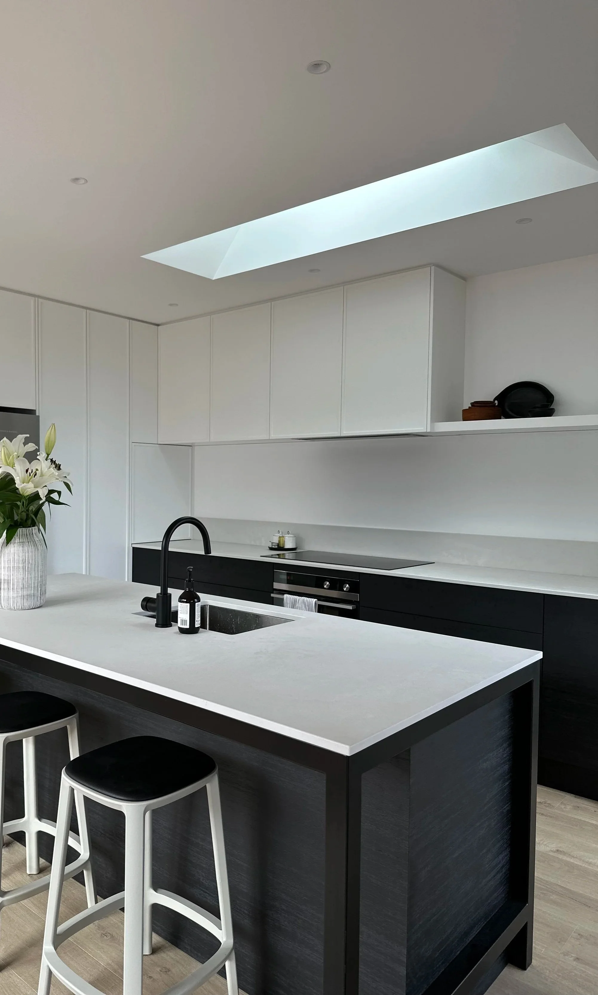 Modern kitchen with white upper cabinets, black lower cabinets, a large white countertop island, and a skylight in the ceiling.