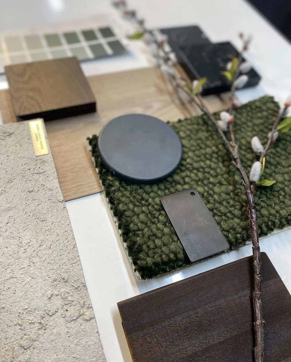 Sample display of interior design materials including wood, fabric, paint, and tile samples along with a branch, a black round object, and a metal keychain