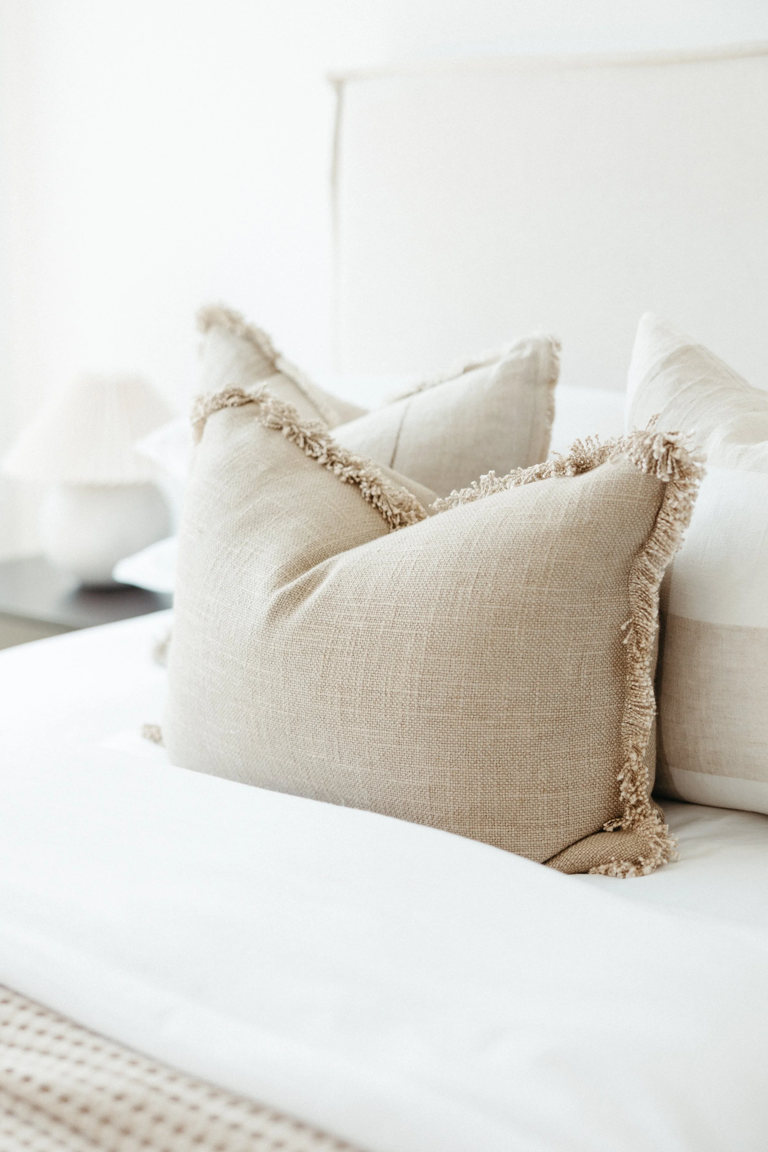 Close-up of beige decorative pillows with fringed edges on a bed.